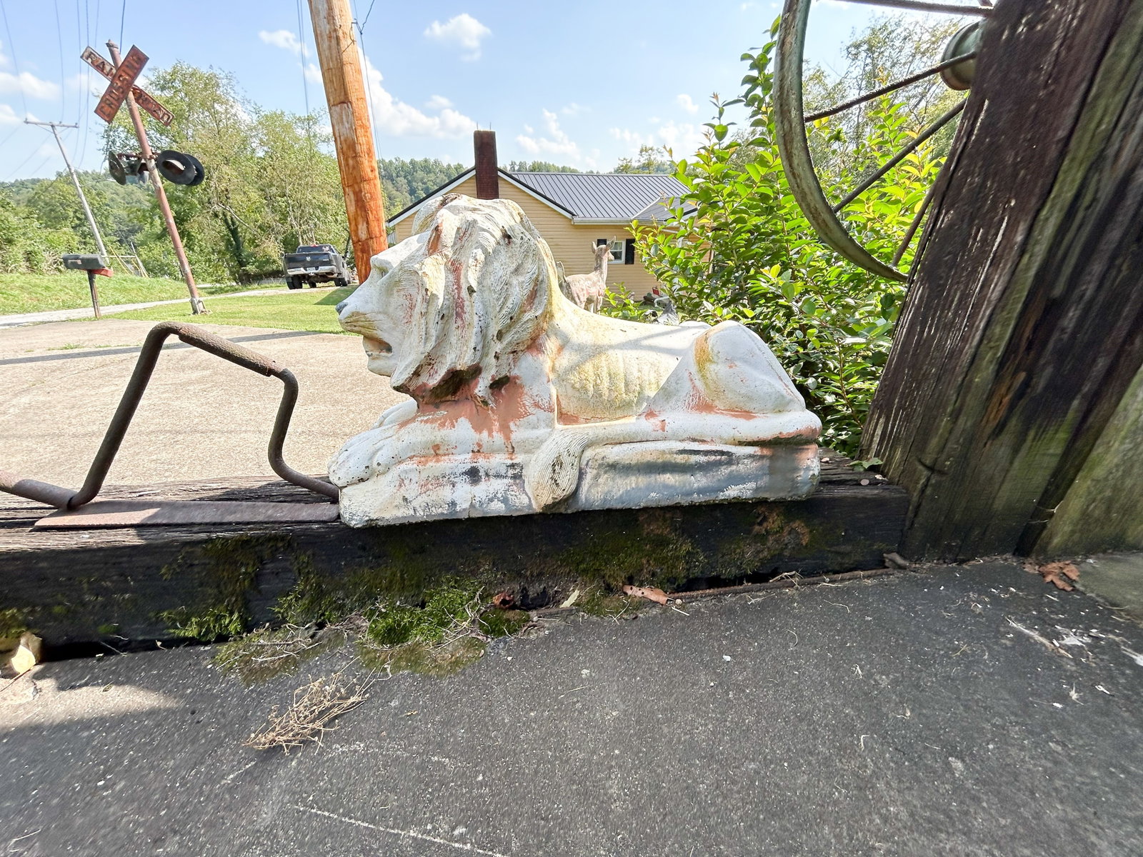 CAST CONCRETE RECUMBENT LION STATUE: Large cast concrete or cast stone garden statue depicting a recumbent lion with a textured mane. The piece features several layers of peeling white and terracotta-toned paint, creating an aged patina.