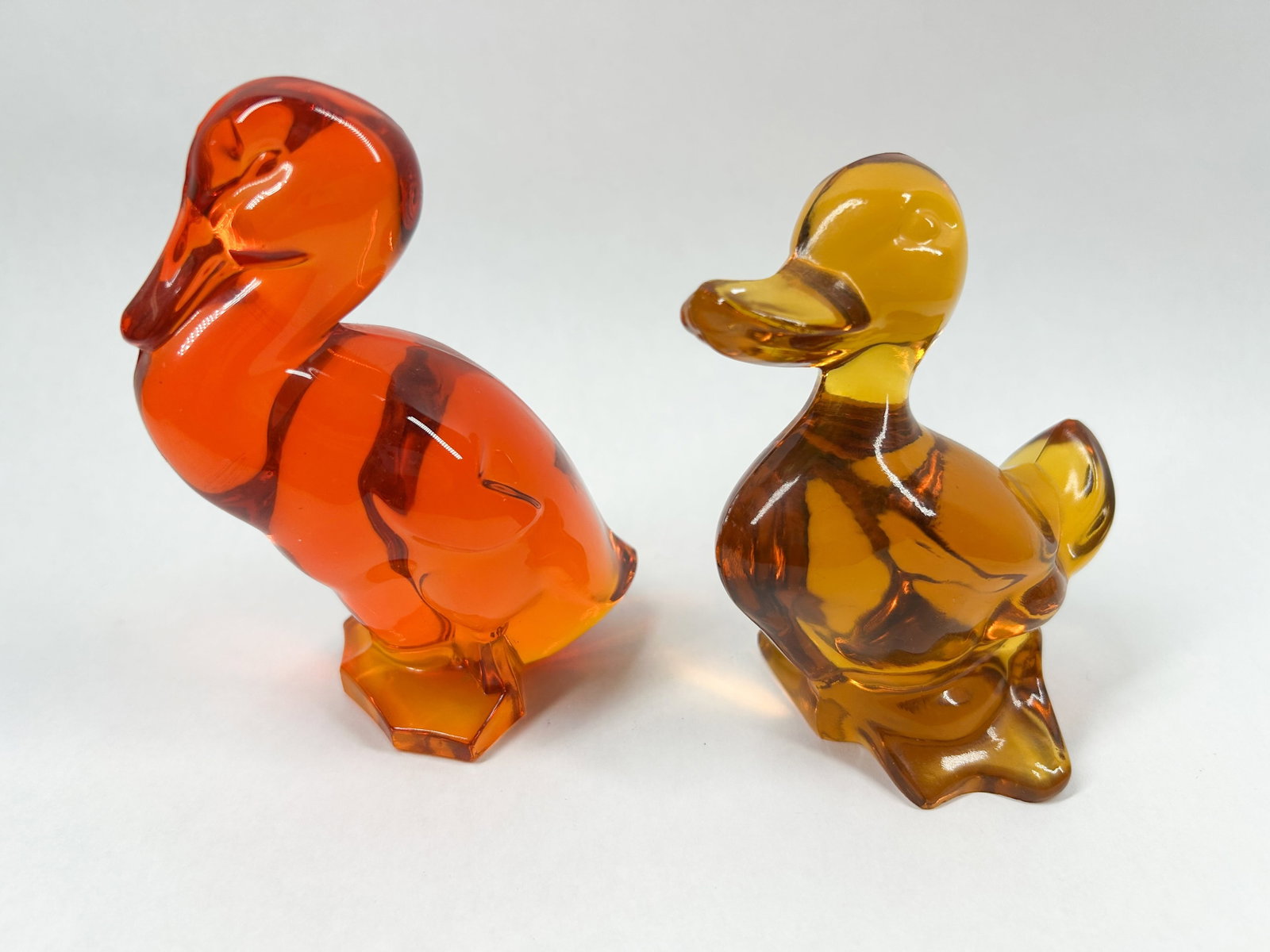TWO VIKING GLASS BIRD FIGURINES: A pair of solid molded glass bird figurines comprising a stylized goose and duckling in orange and amber colorways. The minimalist forms feature flat-ground bases with no visible maker marks or