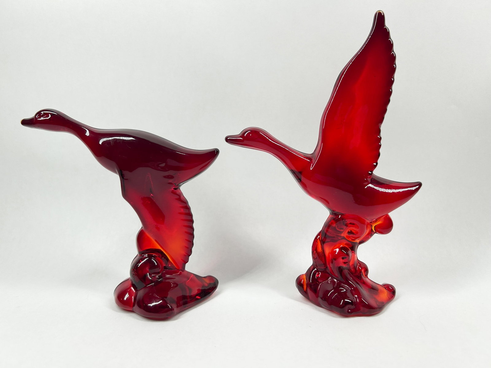 HEISEY BY VIKING RUBY RED GLASS MALLARDS: A pair of bird figurines crafted from translucent ruby red glass. Each stylized avian form is depicted in flight upon an integral organic base.