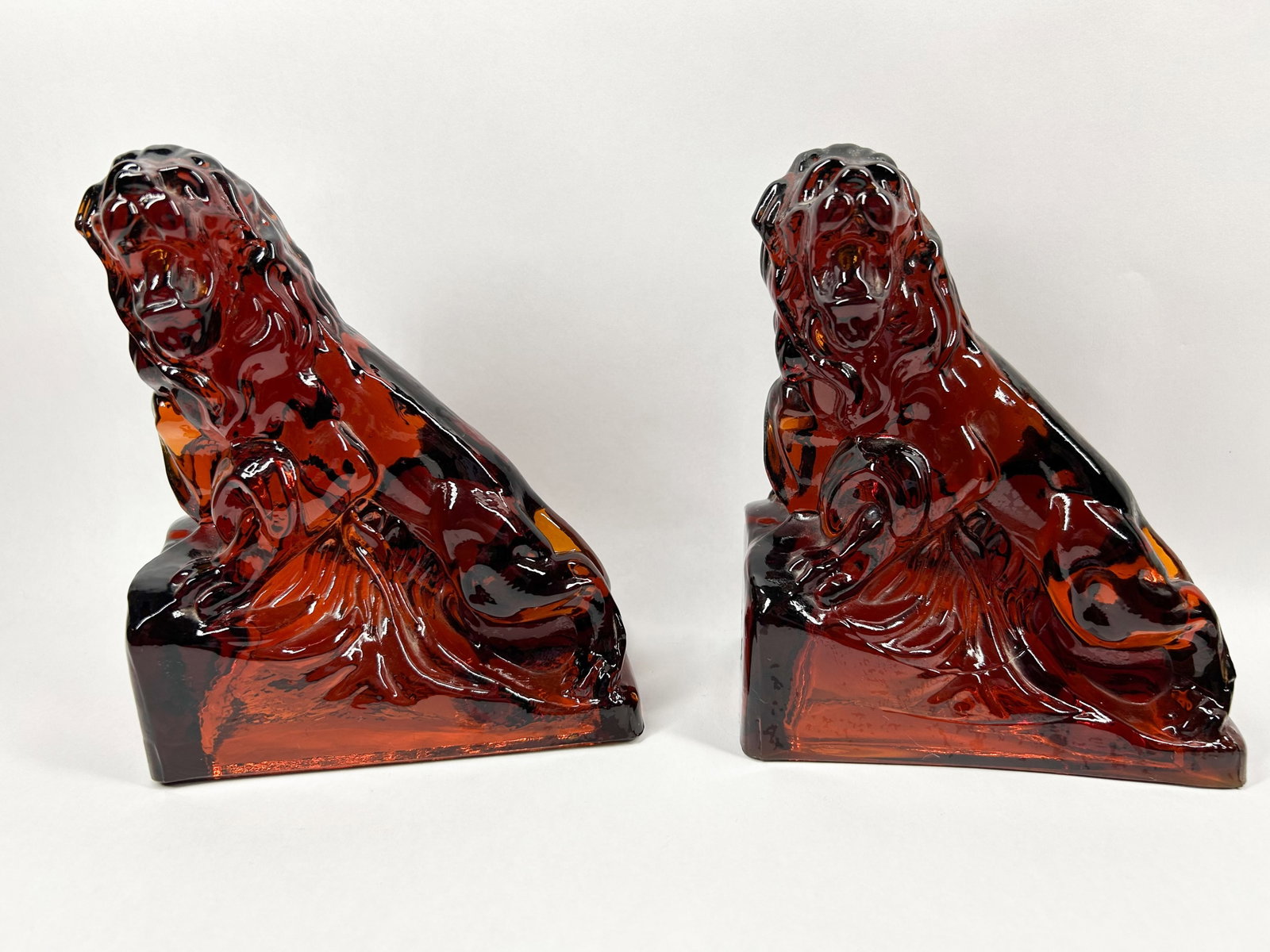 IMPERIAL AMBER LION BOOKENDS: A pair of translucent amber pressed glass bookends, each molded in the form of a seated roaring lion. The figures feature detailed manes and tails that wrap around the back of the integral rectangular