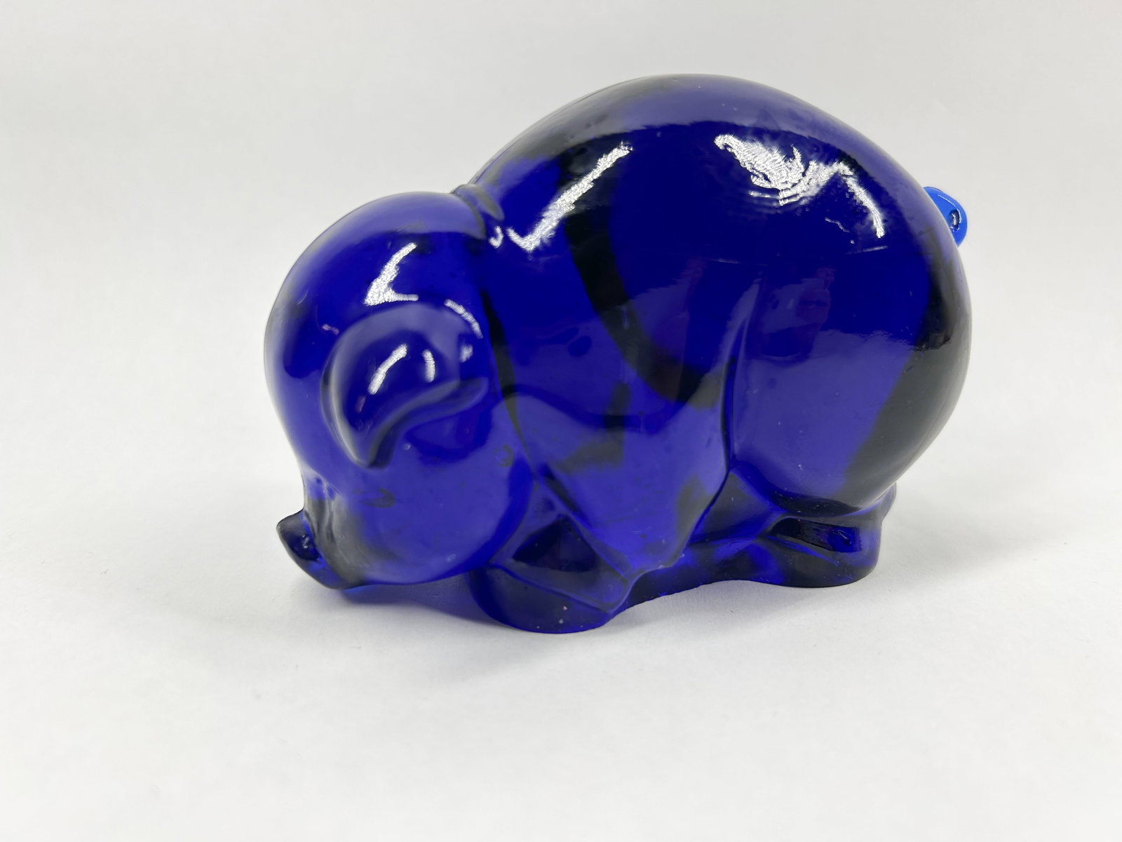 HEISEY BY IMPERIAL ULTRA COBALT BLUE MAMA SOW: A molded cobalt blue glass figurine of a pig in a rooting posture. The translucent glass features dark internal swirls and visible mold seams along the spine and midsection.