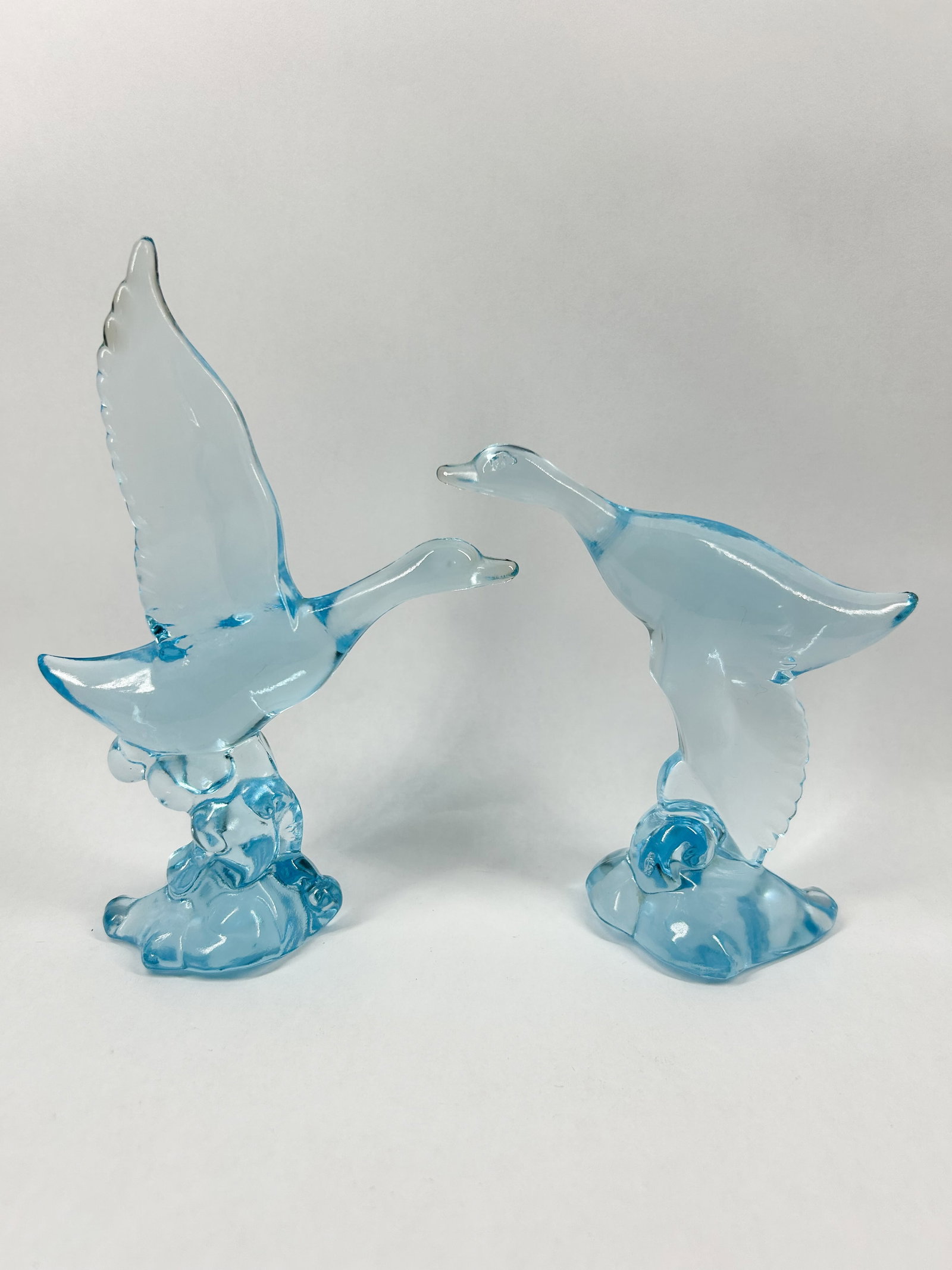 HEISEY BY IMPERIAL HORIZON BLUE MALLARDS: A pair of molded light blue translucent glass figurines depicting mallard ducks in flight, featuring one wings-up and one wings-down pose on stylized wave bases. No maker marks, signatures, or labels 