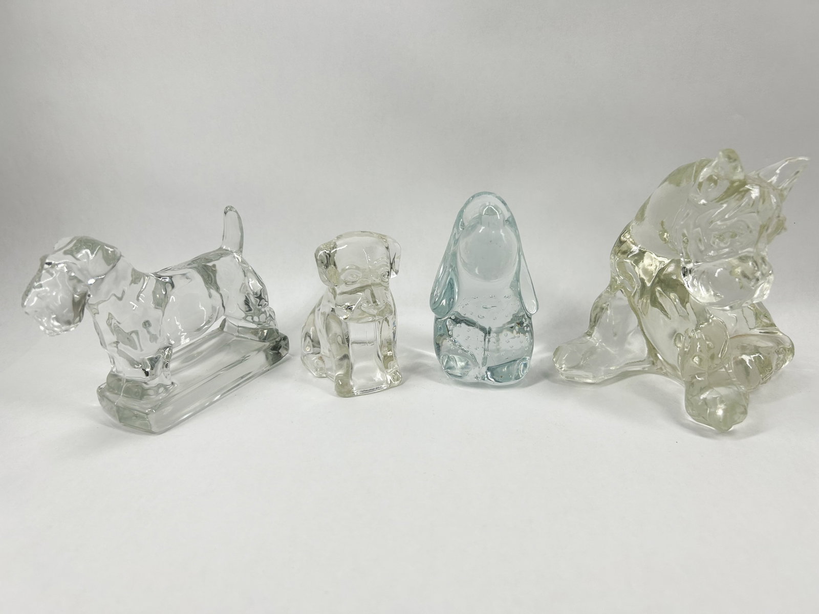 COLLECTION OF GLASS DOG FIGURINES: A collection of molded glass dog figurines in various breeds and finishes. The group includes clear glass terrier and puppy figures alongside a stylized blue glass hound featuring internal controlled