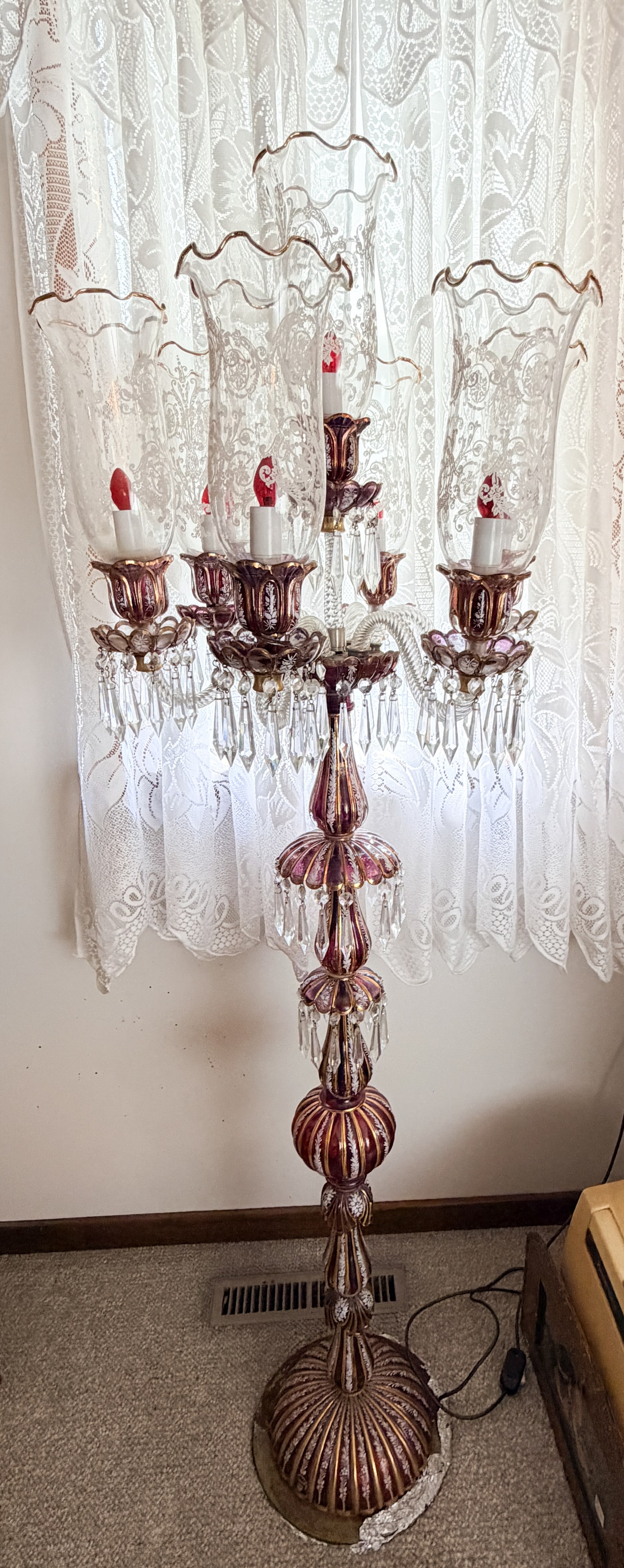 ENAMELED RUBY GLASS FLOOR LAMP: A five-light floor lamp constructed from stacked ruby cased glass sections featuring hand-painted white enamel floral motifs and gilded accents. Scrolled twisted clear glass arms support matching bobe