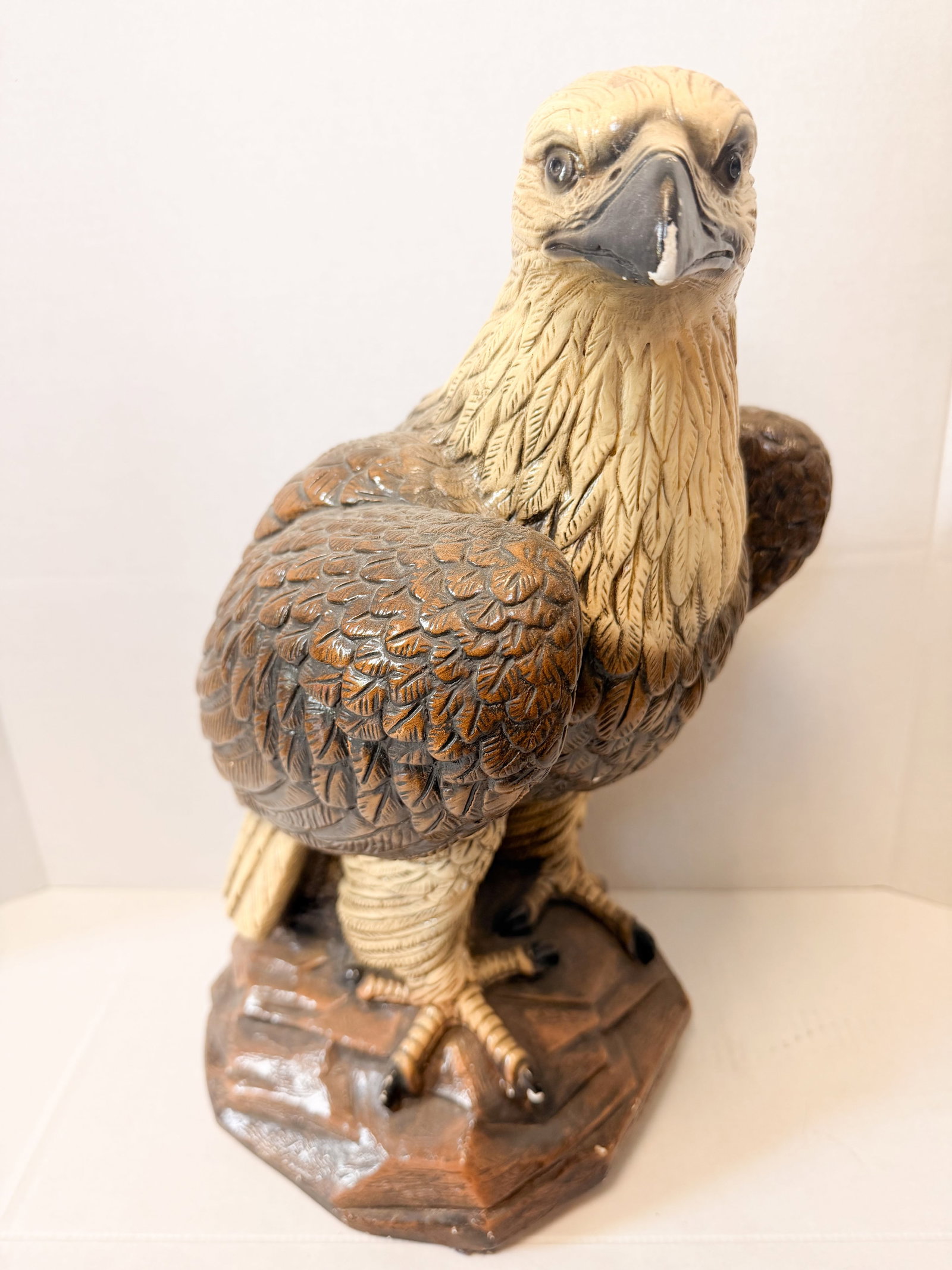 LARGE RESIN PERCHED EAGLE SCULPTURE: Resin perched eagle sculpture rendered with high-relief feather detailing. The figure features a cream-colored head and neck transitioning to a variegated brown body atop a rocky base.