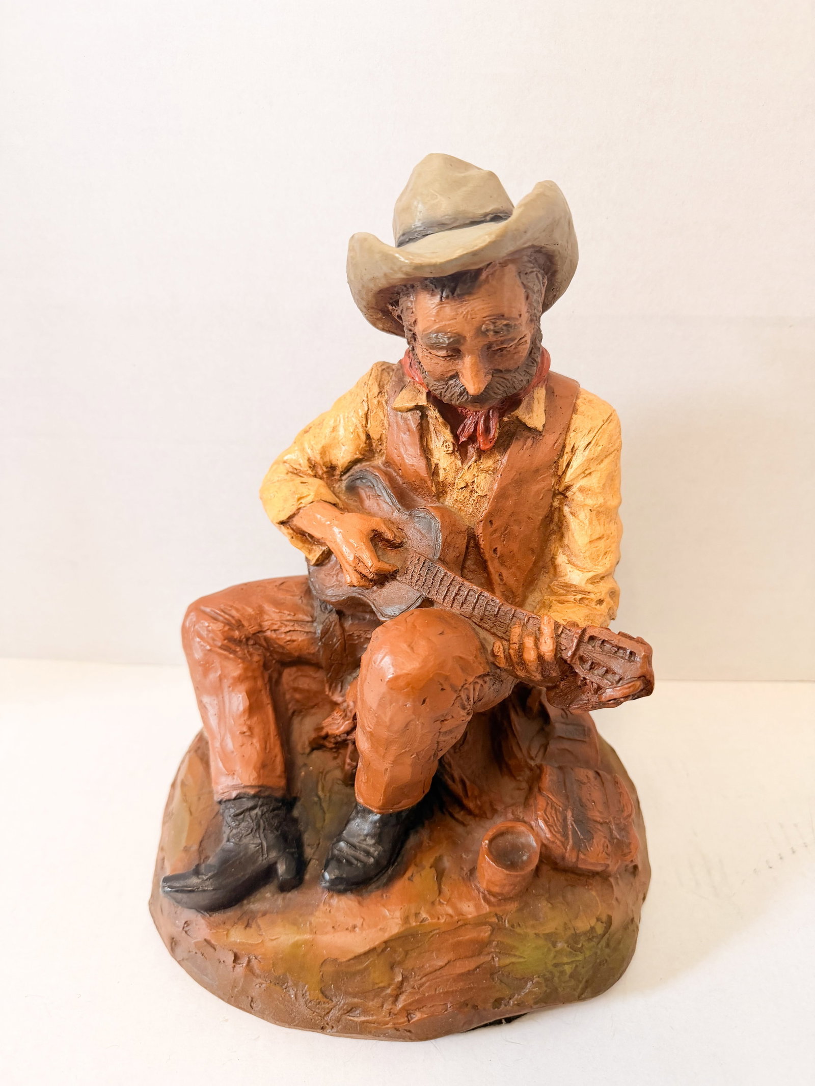 UNIVERSAL STATUARY CORP COMPOSITE COWBOY 1984: Seated cowboy musician figurine produced by Universal Statuary Corp in Chicago. The piece is constructed from cold-painted cast composite material textured to resemble carved wood and bears an embosse