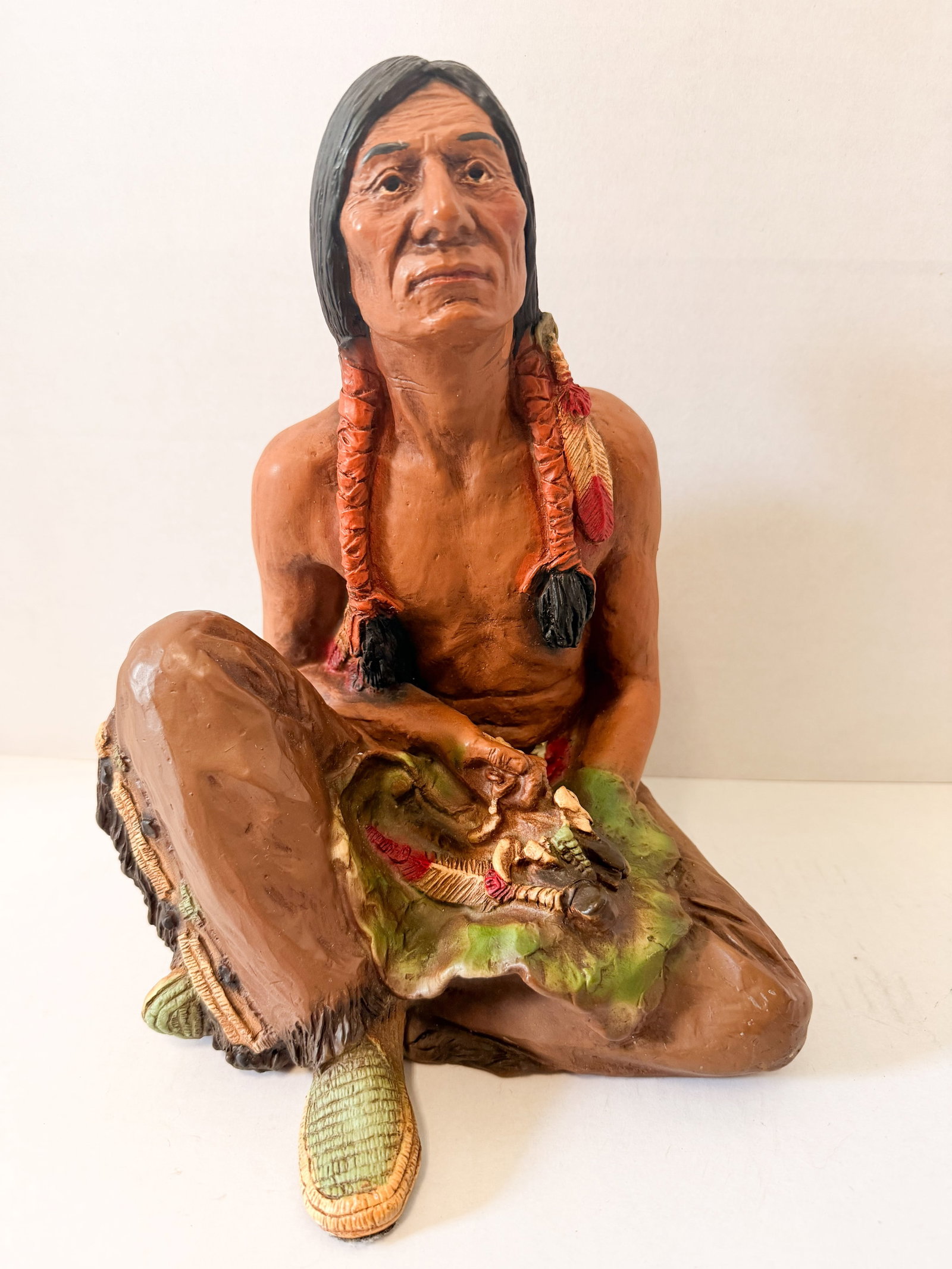UNIVERSAL STATUARY COMPOSITE FIGURE, 1985: A 1985 Universal Statuary Corp molded composite polychrome figurine of a seated Native American man. The reverse base of the red loincloth is impressed with characters reading ?1985, Universal