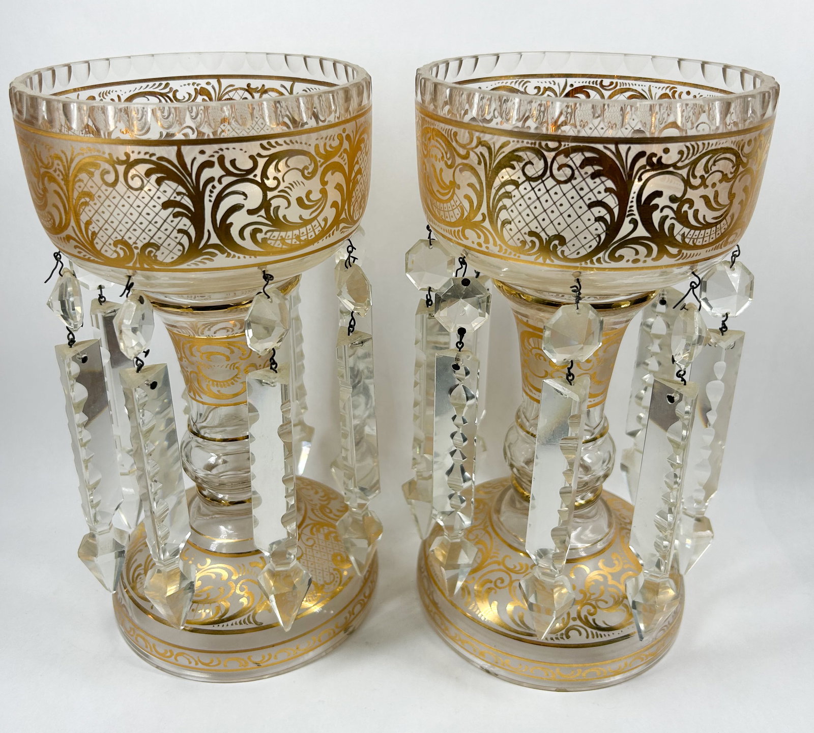 BOHEMIAN GILDED GLASS MANTLE LUSTRES: A pair of Bohemian clear glass mantle lustres featuring scrolling foliate gilding and sawtooth-cut rims. No maker marks or signatures are present on either piece.