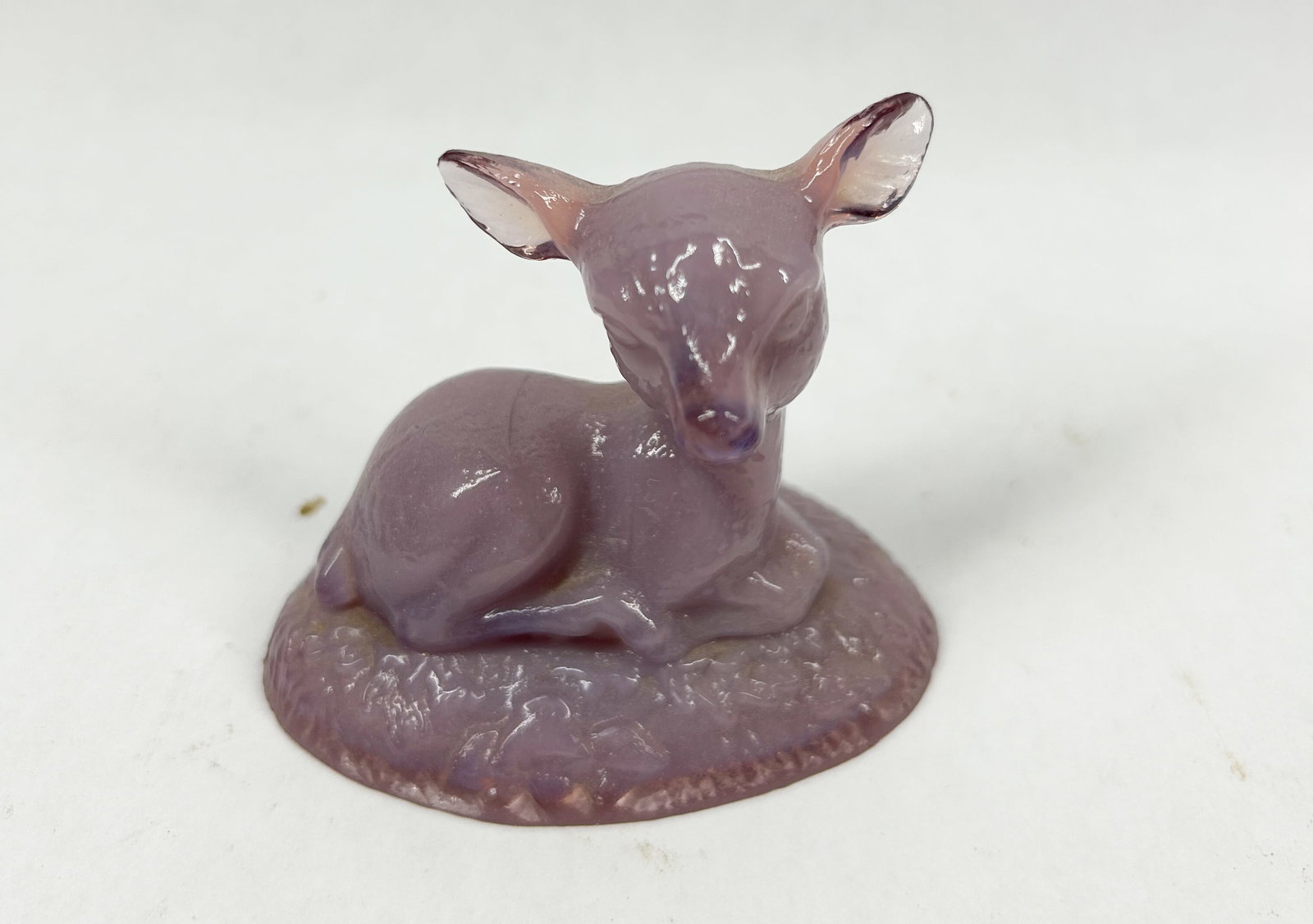 BOYD LAVENDER BINGO DEER: A miniature molded figurine of a recumbent fawn in lavender and white slag glass. The figure is resting on a textured oval base.