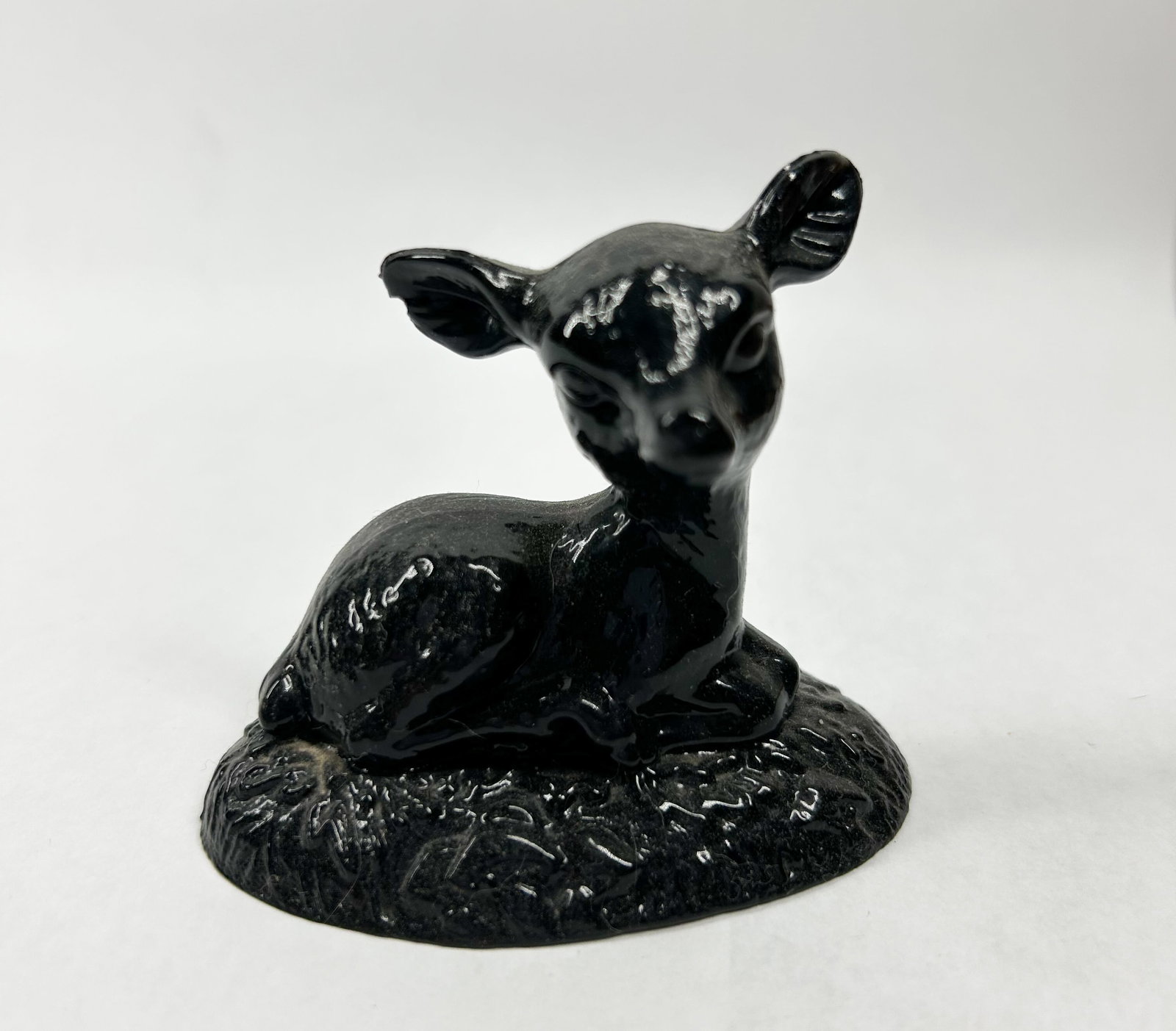 BOYD BLACK BINGO DEER: A stylized figurine depicting a recumbent fawn finished in a high-gloss black glaze. The figure is positioned on an integral, textured oval base and displays mid-century modern aesthetic proportions.