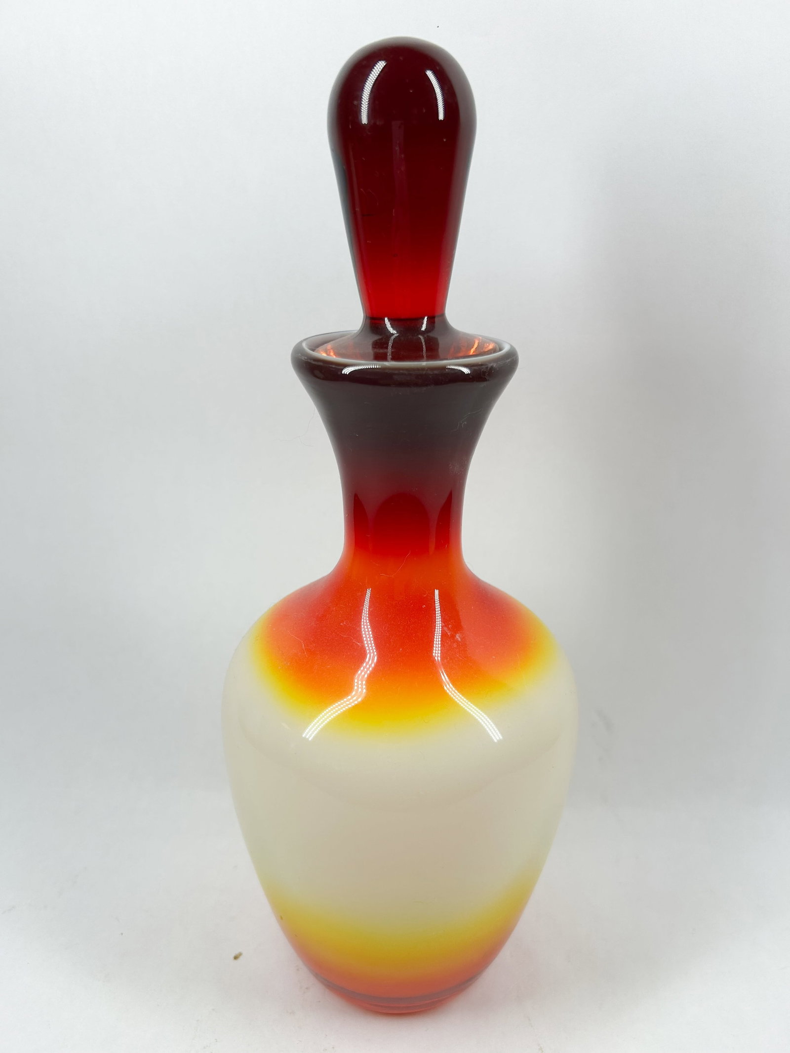 PEACHBLOW DECANTER AND STOPPER, C.1960: Mid-century modern hand-blown cased glass decanter with matching stopper featuring a tri-color sunset gradient over an opalescent white body. No maker marks or signatures are visible.