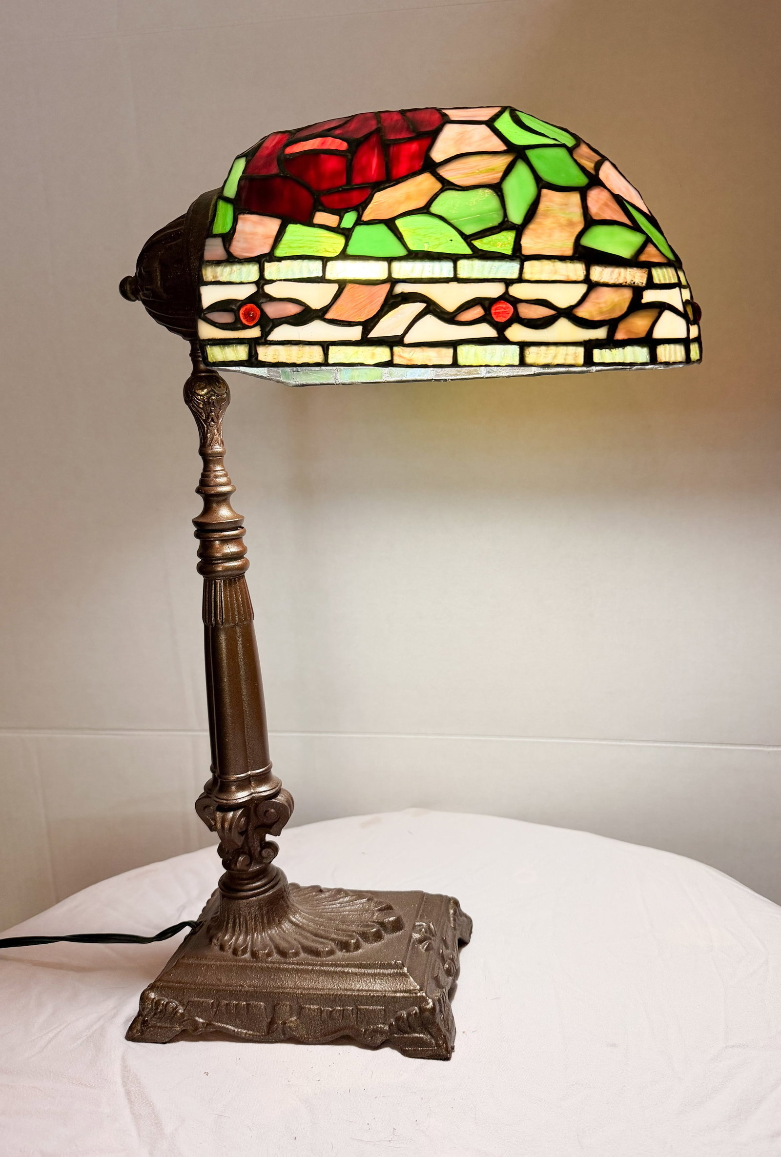 TIFFANY STYLR METAL BANKER LAMP: A banker-style desk lamp featuring a floral rose-patterned slag glass shade assembled using the copper foil technique. The shade is supported by a cast metal base with a bronze-toned patina and an adj