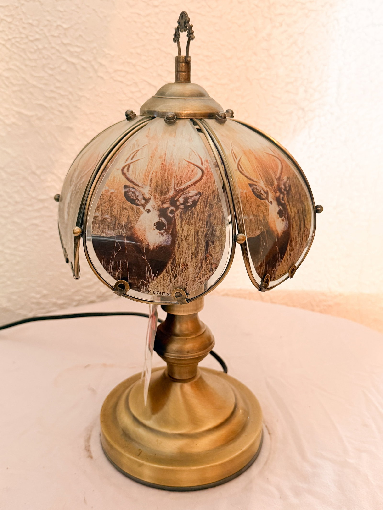 OK LIGHTING DEER GLASS PANEL LAMP: OK Lighting table lamp featuring a brass-toned metal base and six curved glass panels decorated with photorealistic buck deer imagery. A printed mark reading OK LIGHTING is visible along the lower