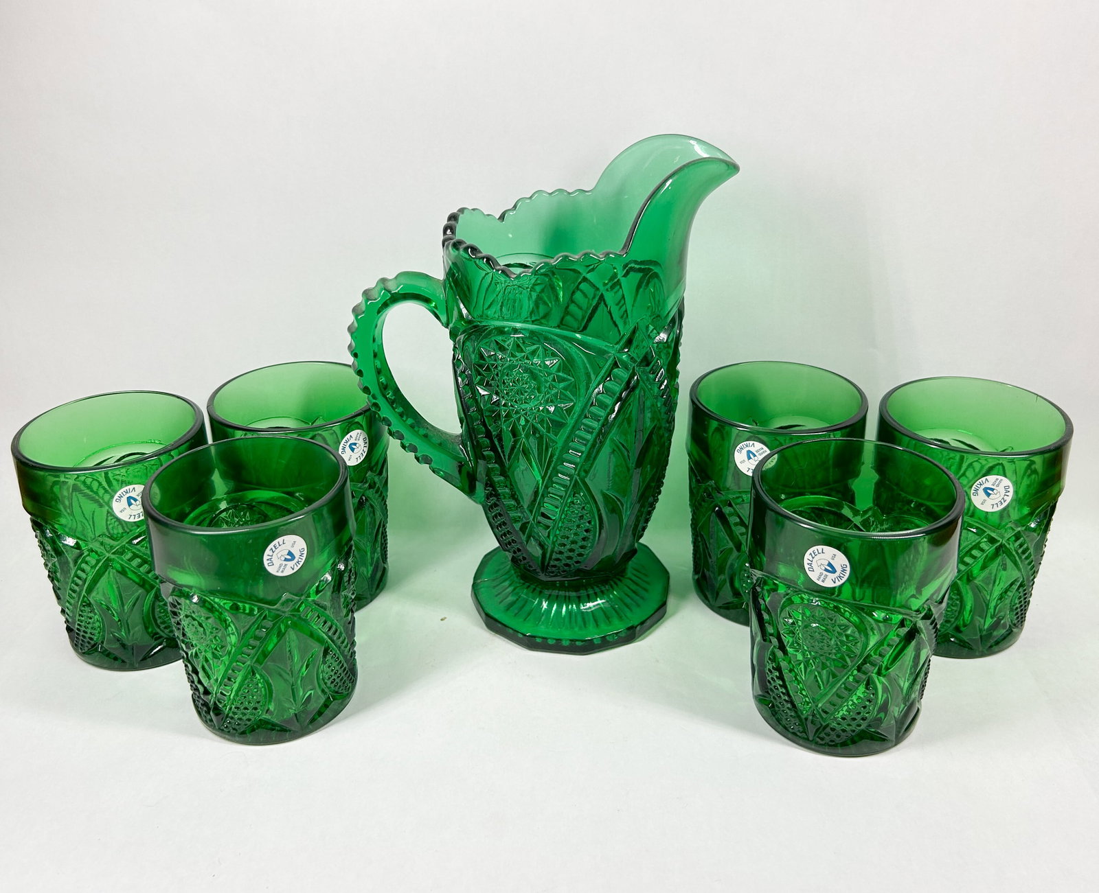 DALZELL-VIKING EMERALD GREEN GLASS SET, 1990S: An American Dalzell-Viking pressed emerald green glass water set comprising one pitcher and six tumblers featuring hobstar and fan motifs. Each piece retains a white oval adhesive label printed in