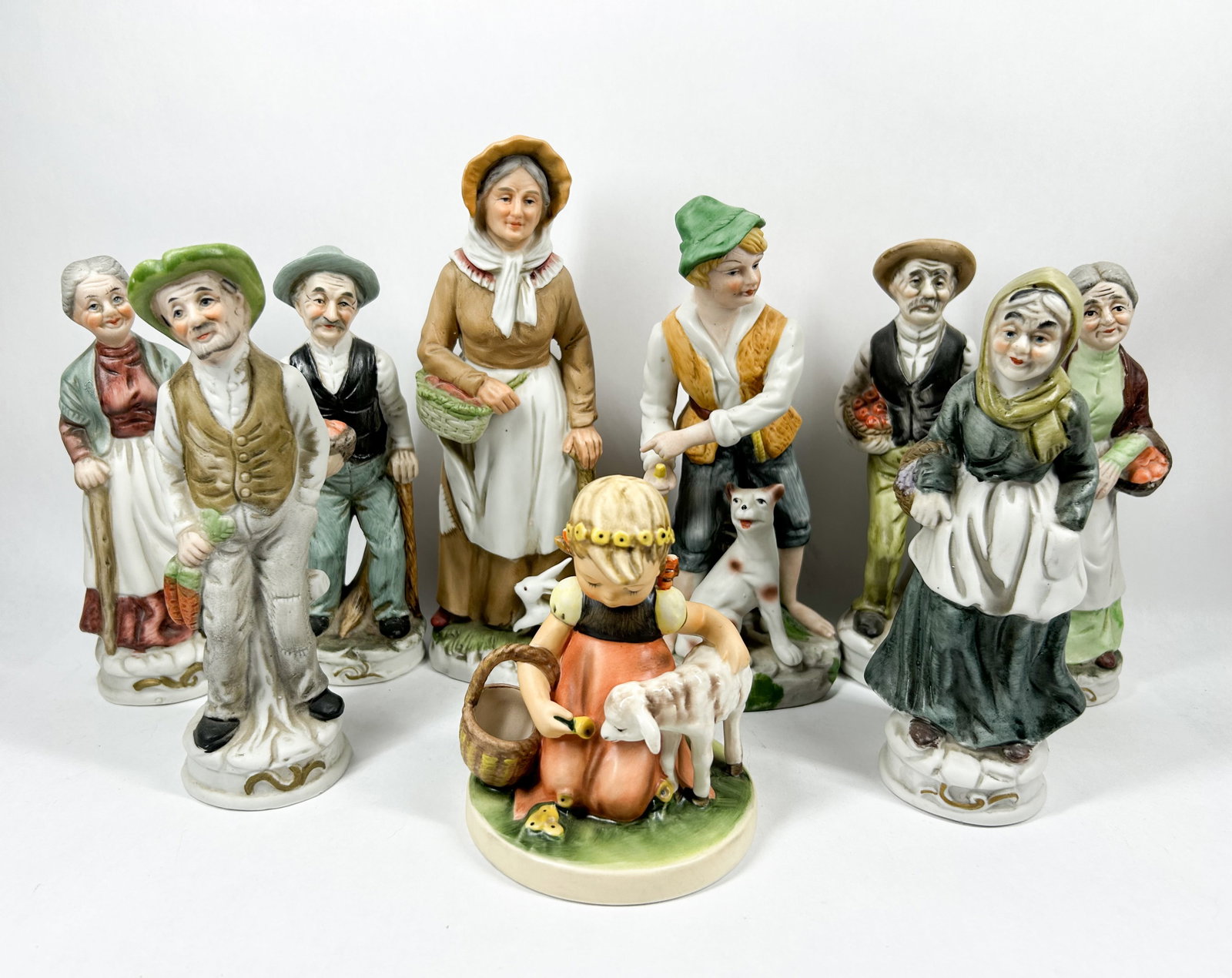 NINE HAND-PAINTED BISQUE FOLK FIGURINES: A group of nine hand-painted bisque porcelain figurines depicting various rustic European characters in traditional attire. The figures feature detailed folk-art painting with a matte finish.