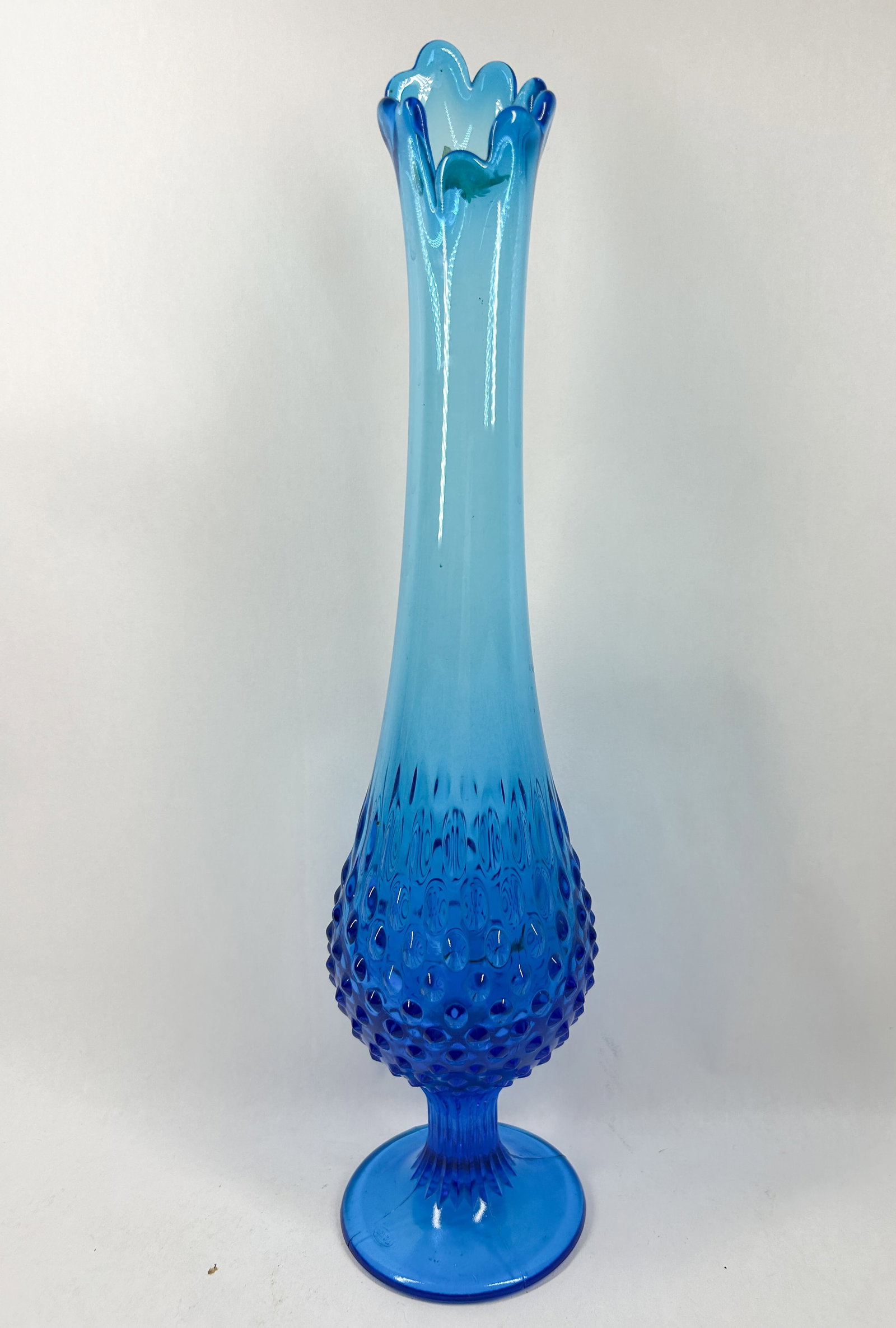 BLUE HOBNAIL SWUNG GLASS VASE 1960S: A mid-century modern swung glass vase in translucent blue featuring a molded hobnail pattern and flared finger rim. A small rectangular label is adhered to the interior rim, but the text is not legibl