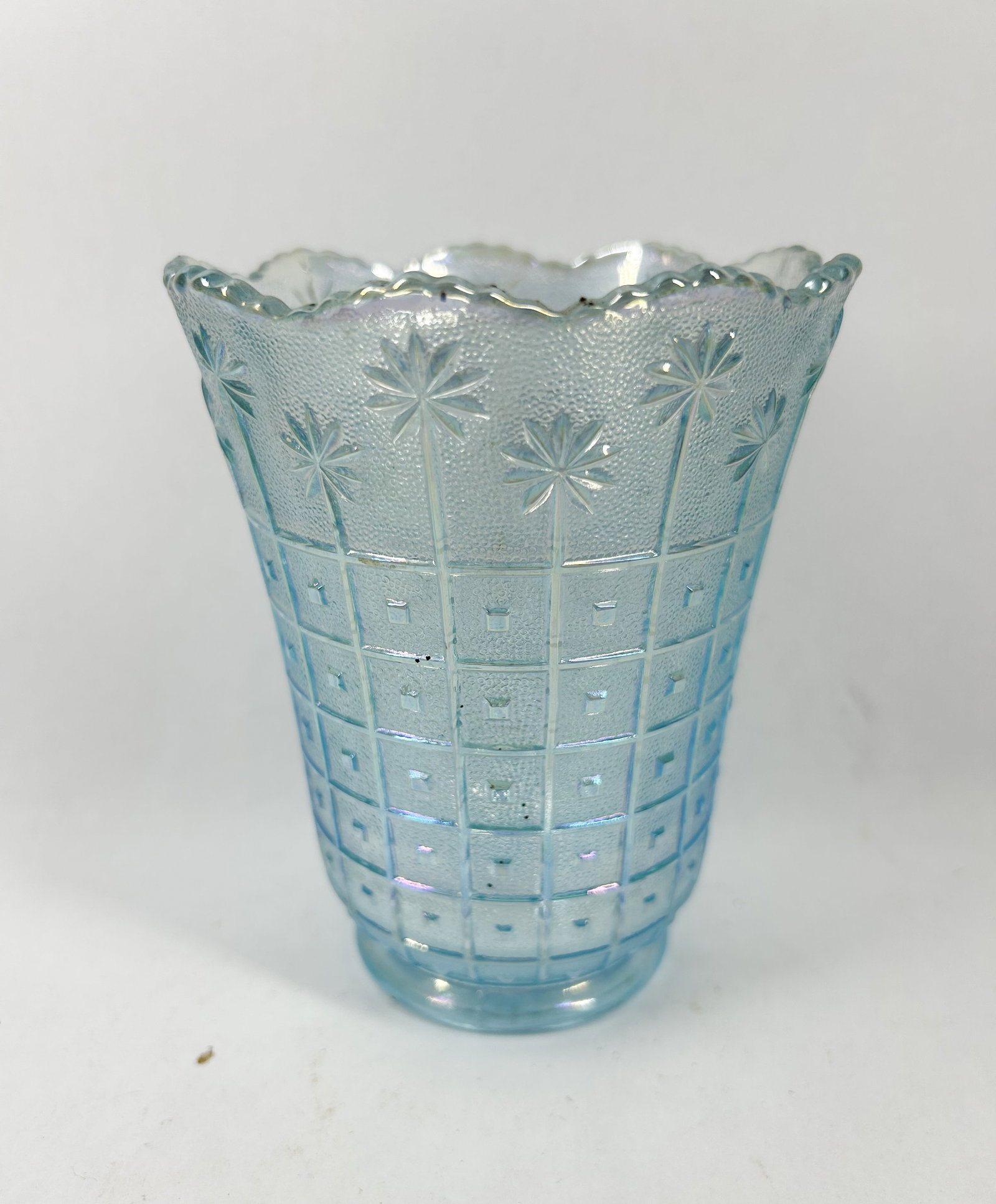 ICE BLUE CARNIVAL GLASS VASE: Pressed glass vase featuring an iridescent ice blue finish and Star and Lattice pattern. The vessel displays stylized floral motifs above a geometric grid with a stippled ground and scalloped rim.