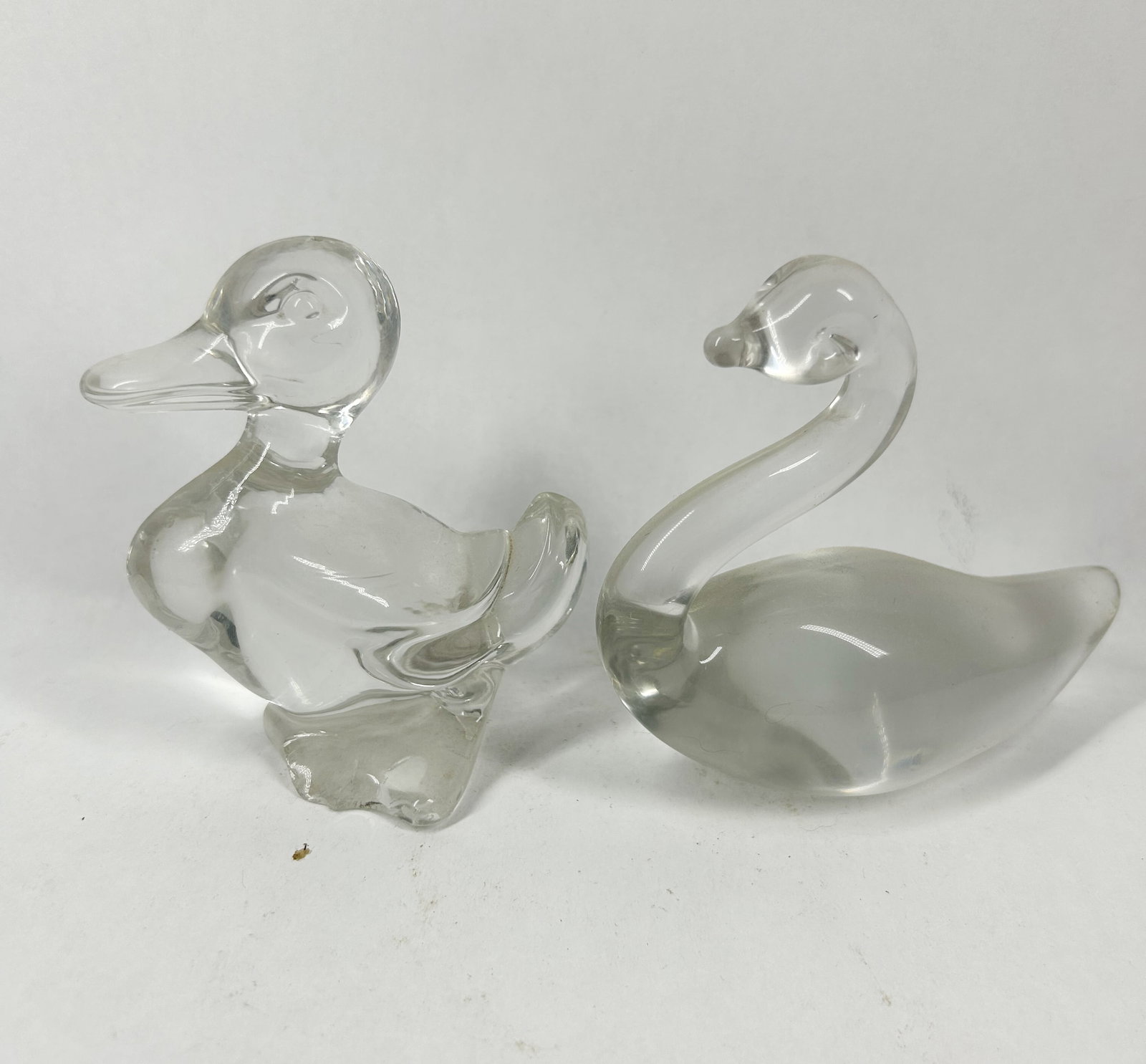 HEISEY CLEAR DUCK AND SWAN: A pair of clear molded glass figurines comprising a standing duck with an upturned tail and a swimming swan with a curved neck. The items are produced from transparent glass and lack identifiable make