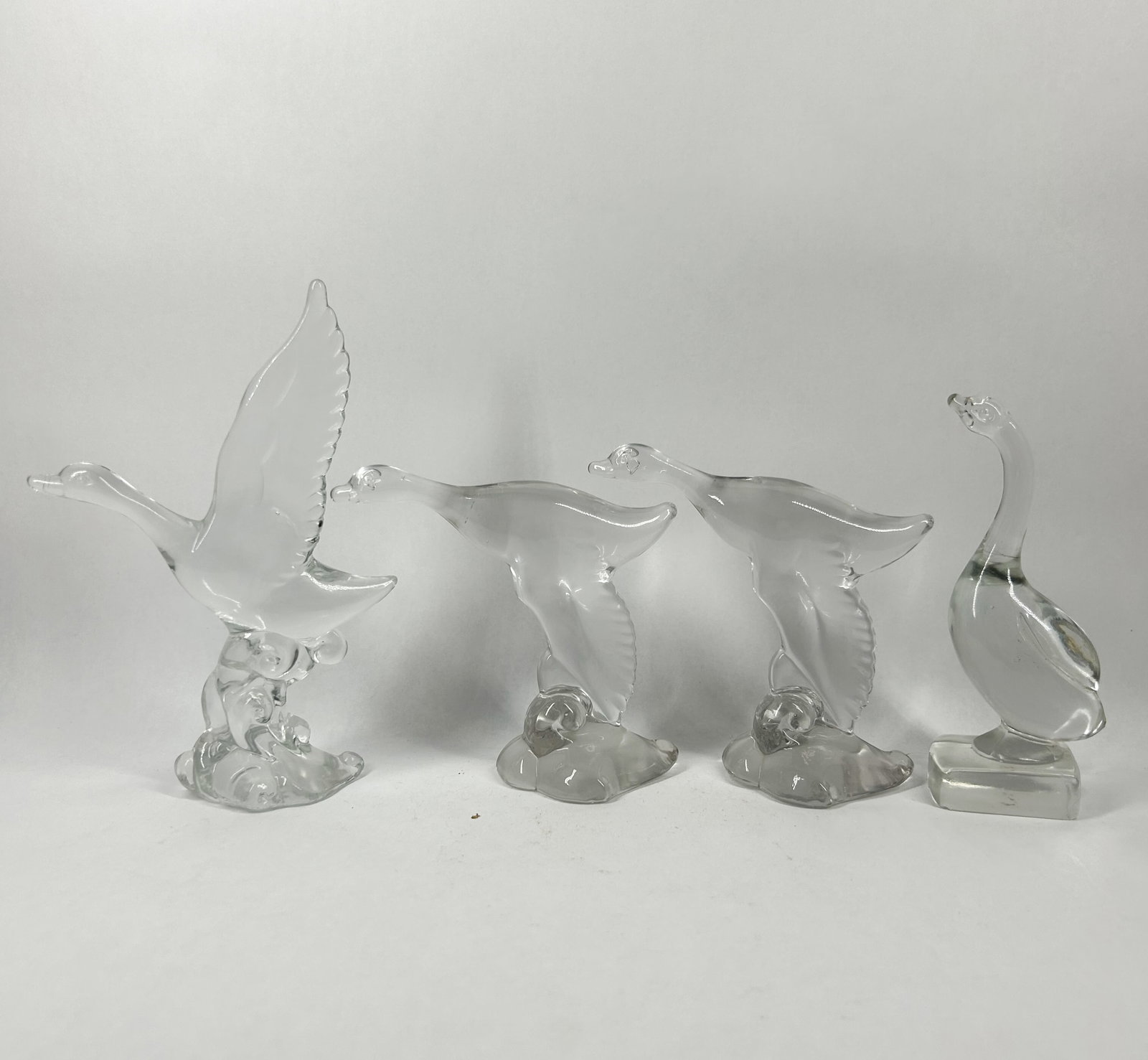 HEISEY MALLARD COLLECTION: A collection of clear glass waterfowl figurines. The figures are modeled in flight and standing poses, featuring textured and smooth rectangular bases. No maker's marks or signatures are visible.