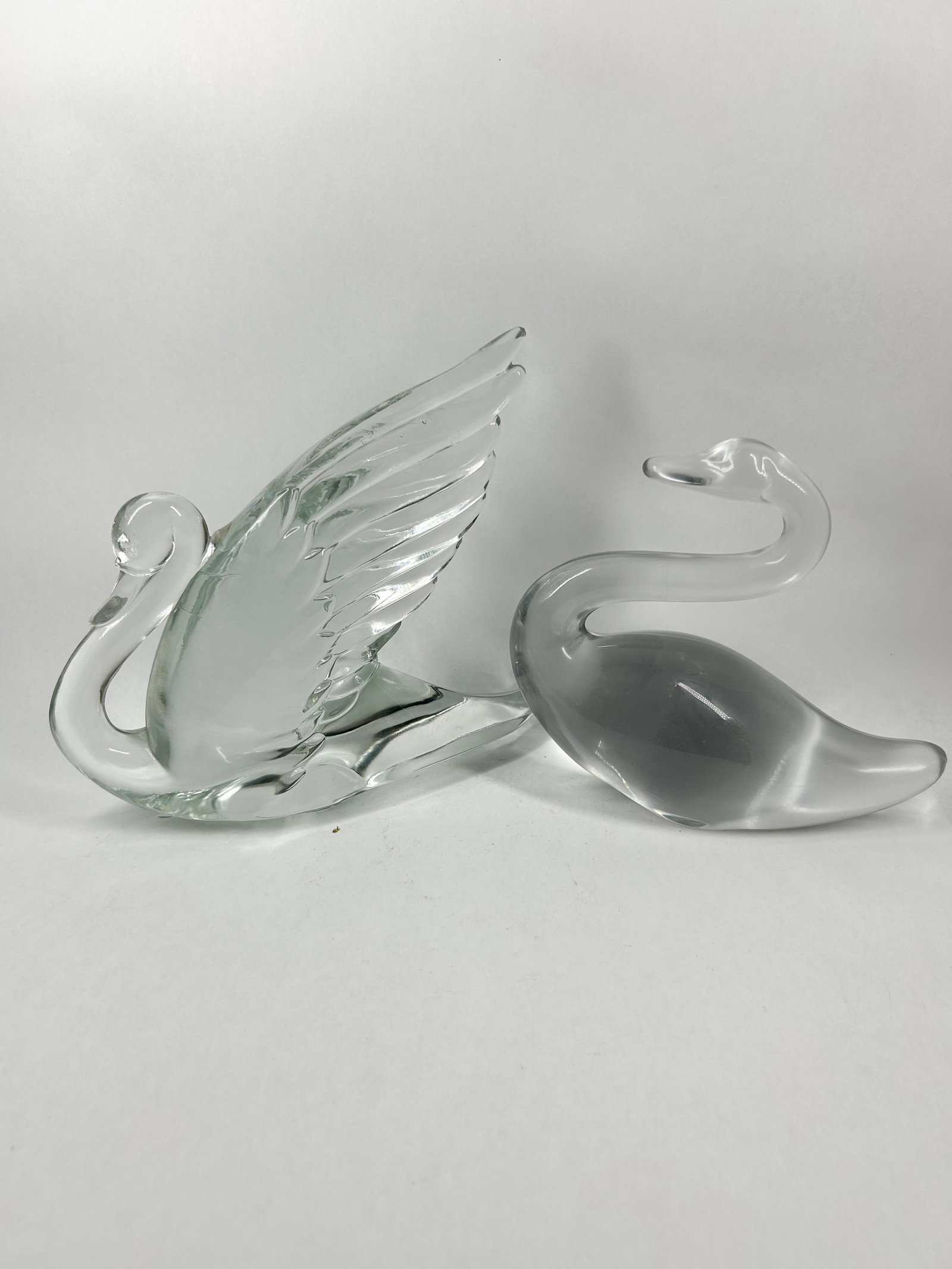 HEISEY CLEAR GLASS SWAN FIGURINES: A pair of solid clear art glass swan figurines of differing designs. One figurine features a textured body with raised, molded wings, while the other exhibits a minimalist, smooth form with a slender 
