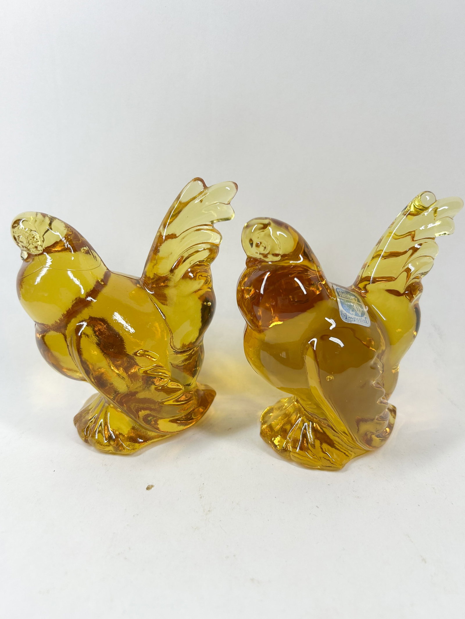 HEISEY BY IMPERIAL AMBER GLASS FIGHTING CHICKENS: A pair of mold-pressed translucent amber glass figurines depicting fighting cocks, produced by the Imperial Glass Corporation using original A.H. Heisey & Company molds. One bird retains a blue and