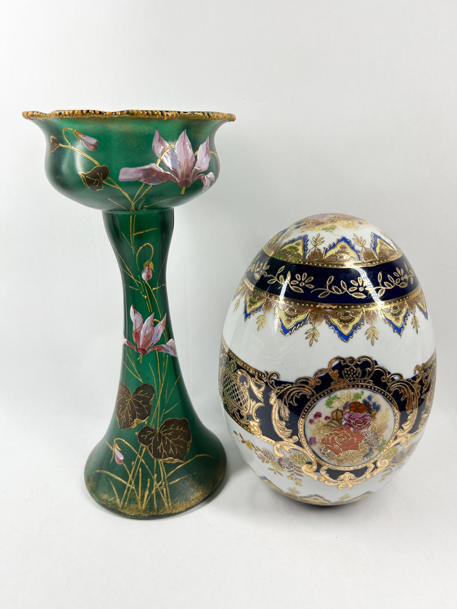 TWO DECORATIVE GLASS AND PORCELAIN ITEMS: A frosted emerald green glass tazza featuring hand-painted cyclamen blossoms and a ruffled gilt-beaded rim is paired with a large porcelain egg-form dresser box decorated with cobalt blue bands and go