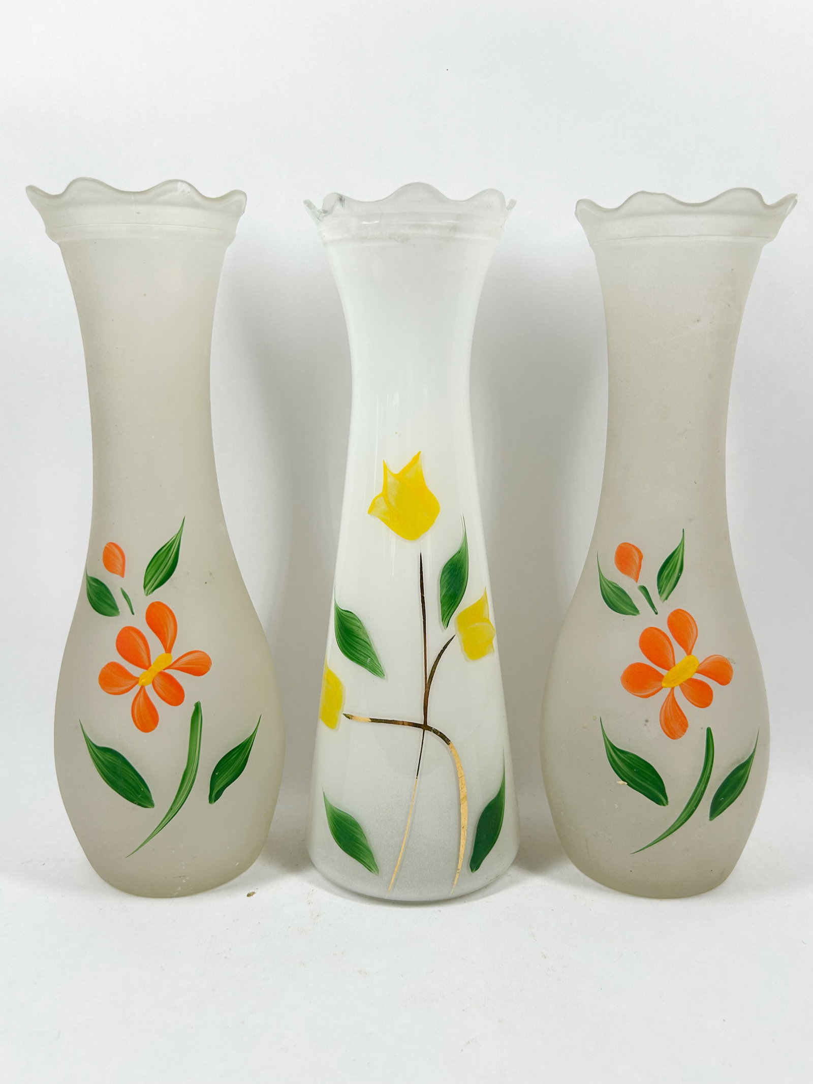 HAND-PAINTED GLASS VASE TRIO, VINTAGE: A vintage trio of glass bud vases comprising a matching pair of frosted vases decorated with orange blossoms and a single milk glass vase featuring yellow tulips. Each piece displays a ruffled