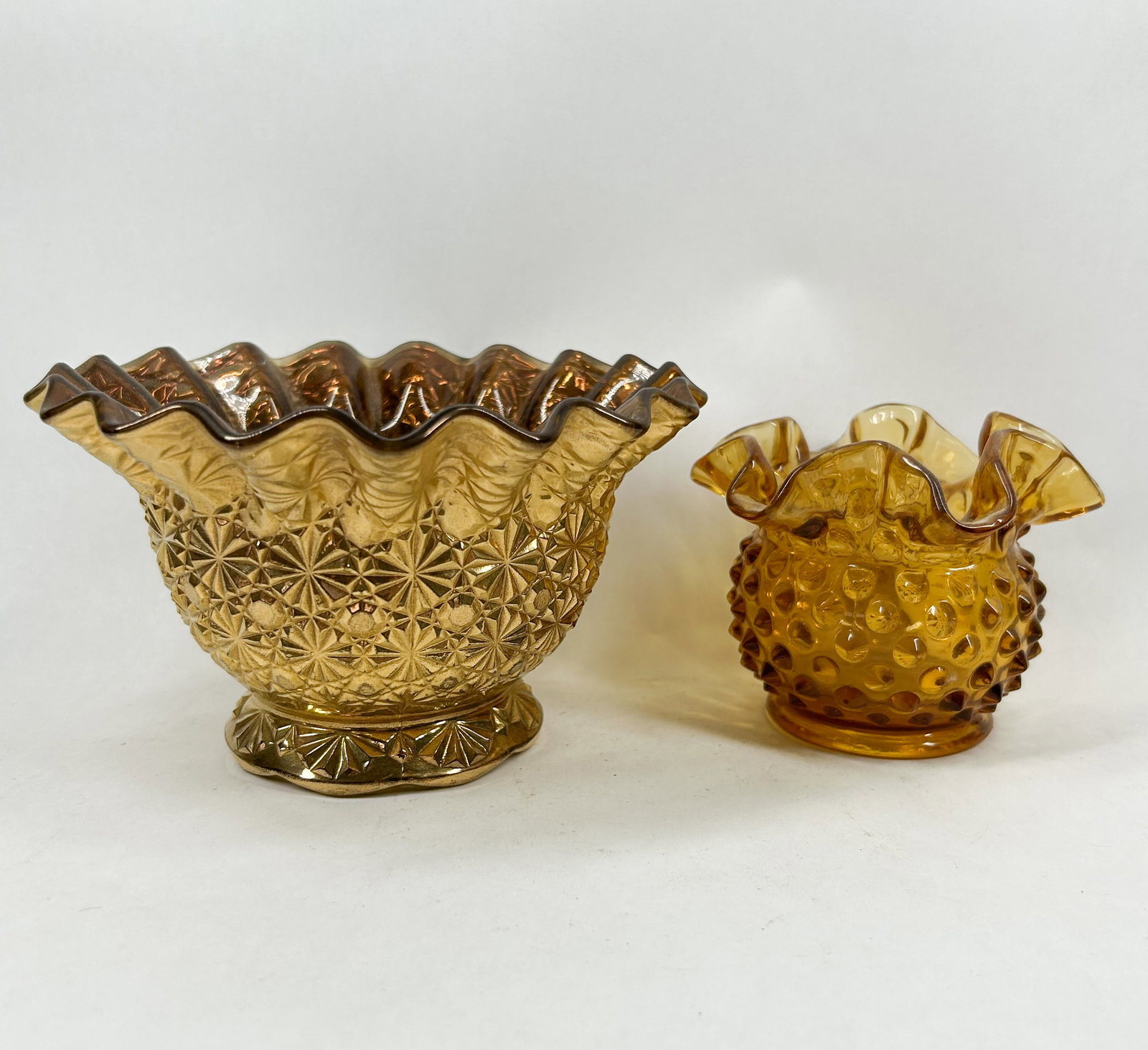 TWO AMBER PRESSED GLASS VESSELS: A pair of amber-toned glass vessels including a marigold carnival glass pedestal bowl with a starburst pattern and a smaller vase with a uniform hobnail texture. Both pieces feature hand-finished