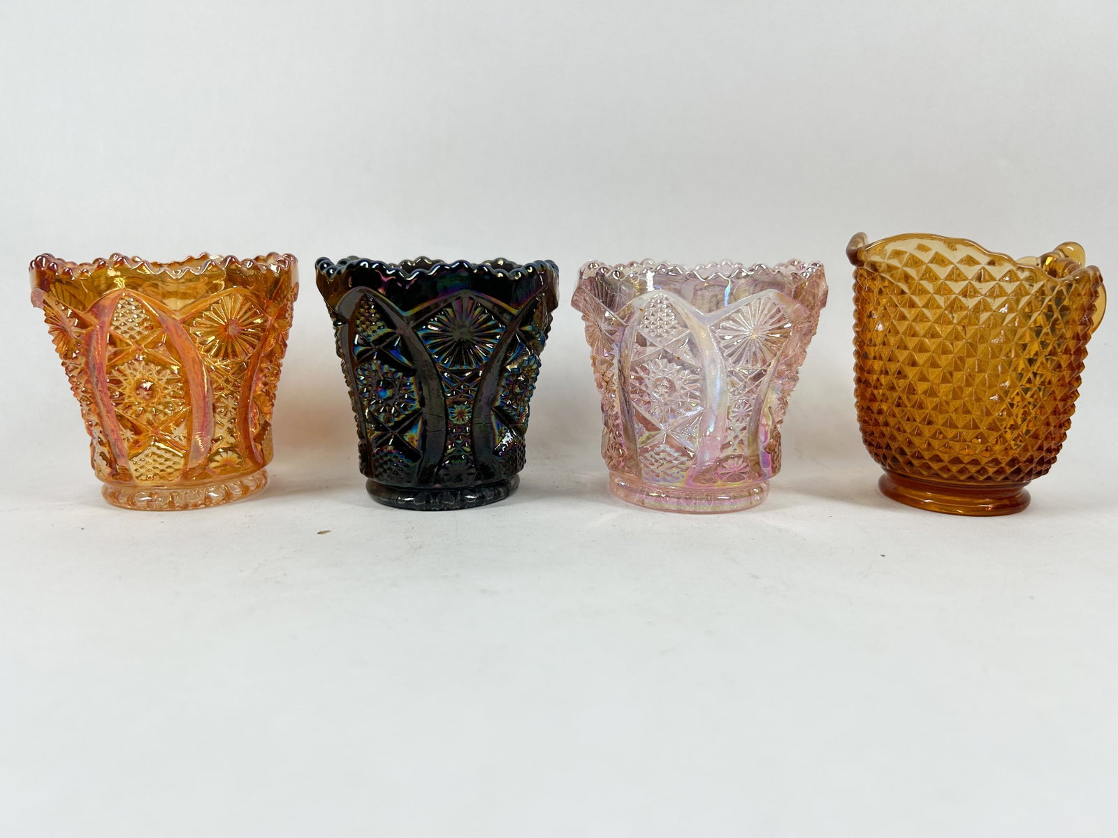 VINTAGE CARNIVAL AND AMBER GLASS TOOTHPICK HOLDERS: An assortment of four vintage pressed glass items featuring three iridescent carnival glass toothpick holders in the Whirling Star pattern and one amber glass creamer in the Diamond Point pattern. No