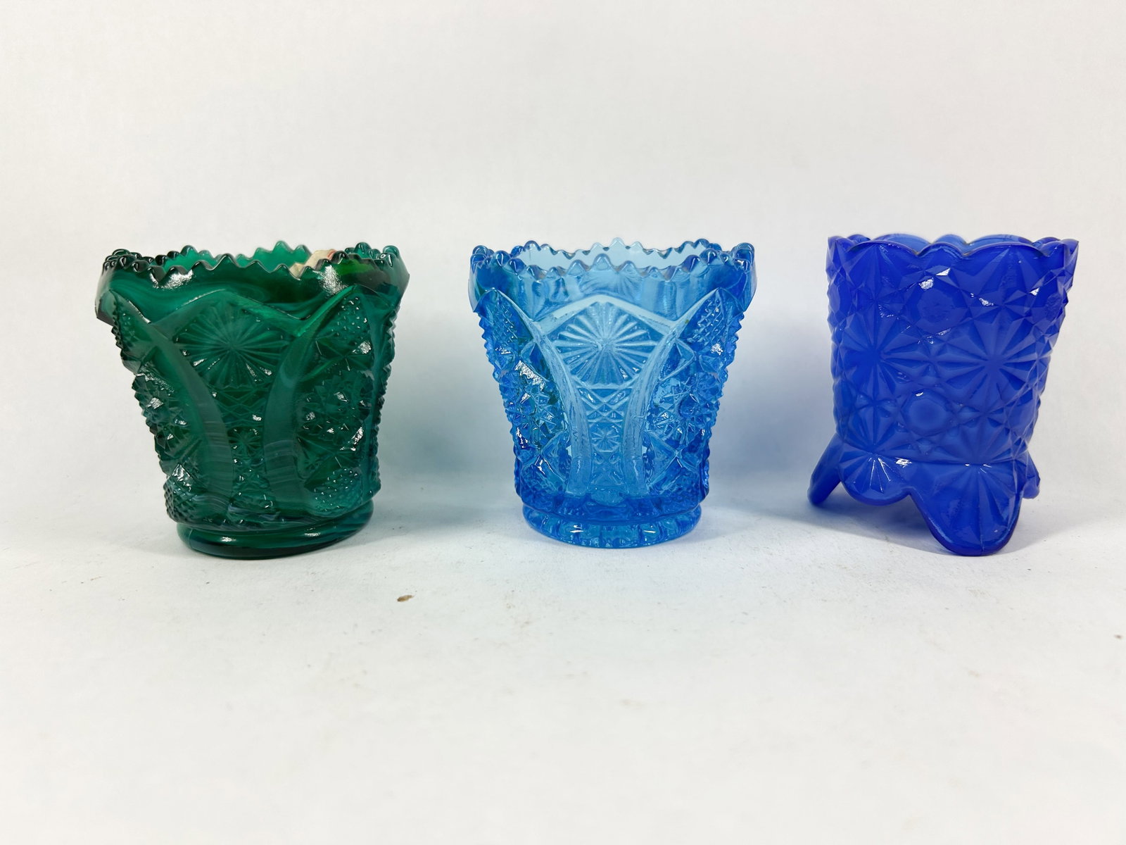 TRIO OF PRESSED GLASS TOOTHPICK HOLDERS: A trio of mid-20th century pressed glass toothpick holders comprising two hobstar and arches examples in green slag and light blue, and a cobalt blue daisy and button pattern holder. A white adhesive