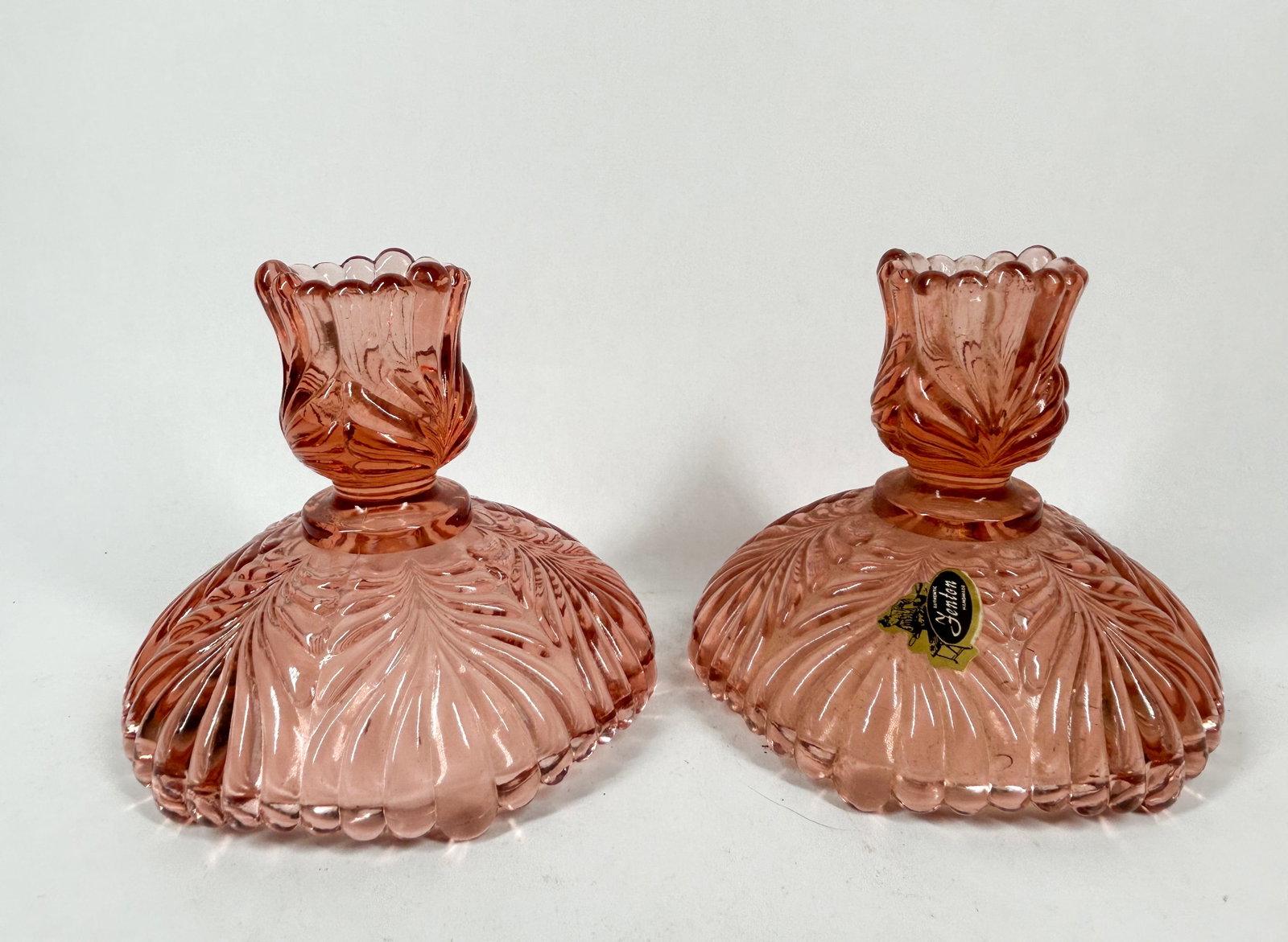 FENTON DUSTY ROSE GLASS CANDLESTICKS, 2000S: A pair of Dusty Rose pressed glass candlesticks in the Plume pattern produced by the Fenton Art Glass Company. The center underside of each base features an impressed mark consisting of the word