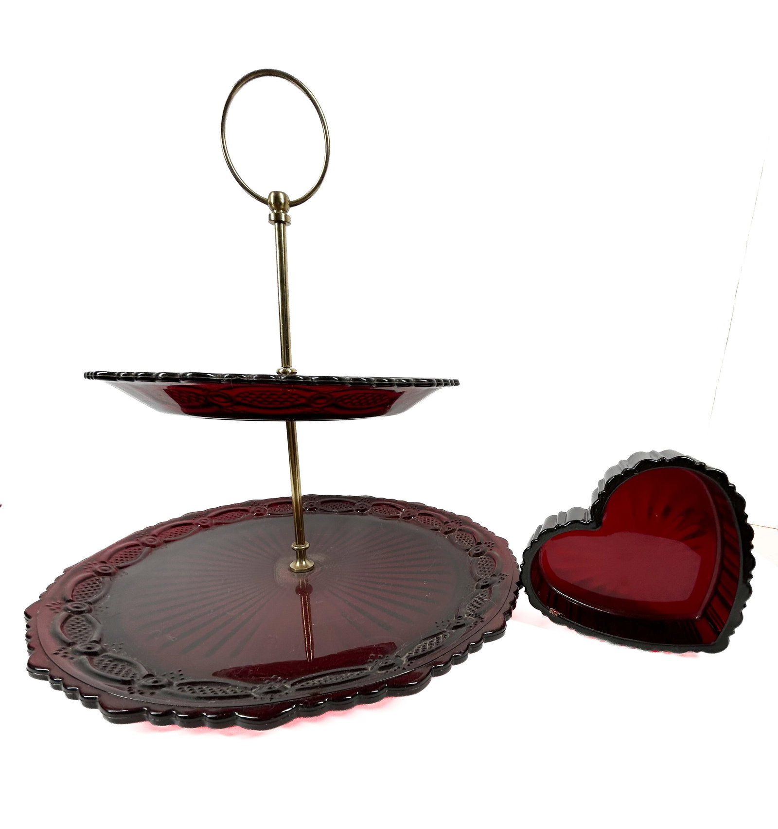 AVON CAPE COD RED GLASS SERVICE: Two pieces of ruby red pressed glass in the Cape Cod pattern by Avon. The set comprises a two-tiered tidbit server with brass-tone metal hardware and a heart-shaped trinket dish.
