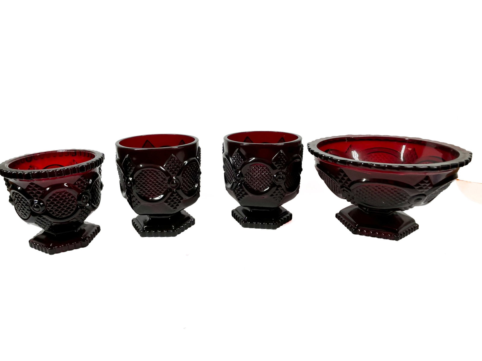 AVON CAPE COD RUBY RED GLASS GROUP: A group of Avon Cape Cod pattern ruby red pressed glass tablewares. A molded mark reading AVON is present on the underside of each square footed base.