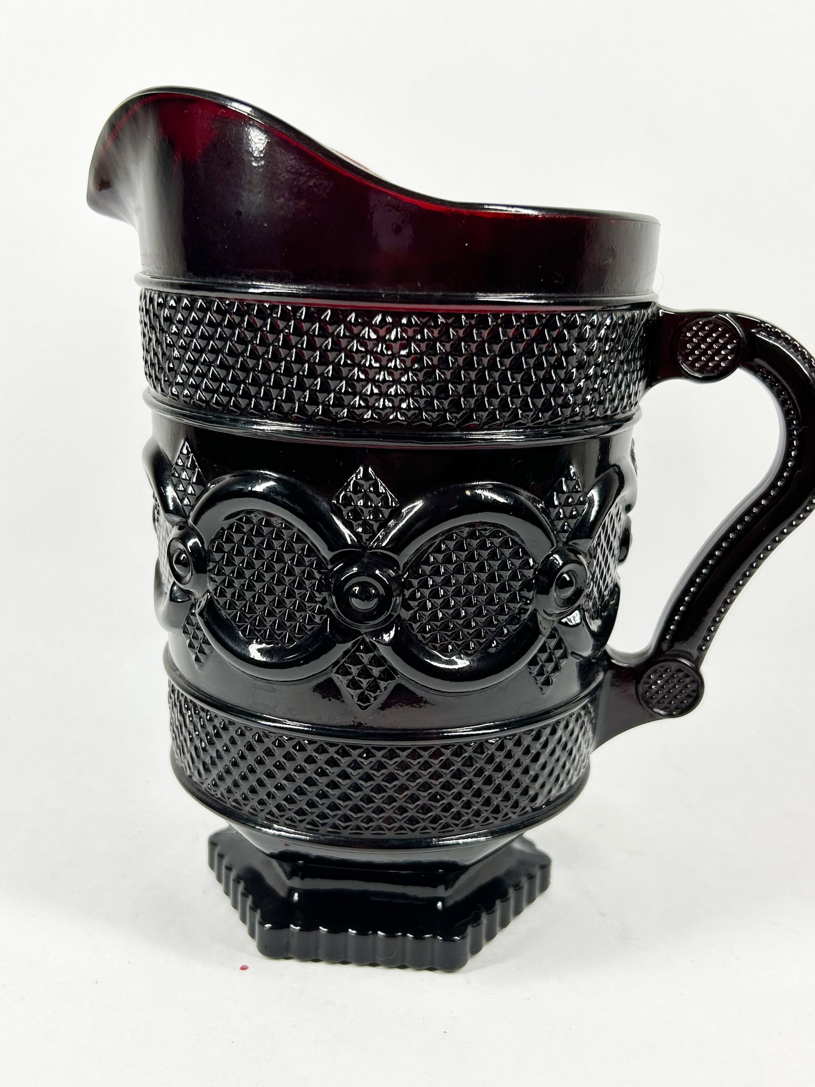 AVON RUBY GLASS CAPE COD PITCHER: Pressed ruby red glass water pitcher in the 1876 Cape Cod pattern. The underside of the octagonal base bears an impressed copyright symbol followed by AVON and the mold number 28.