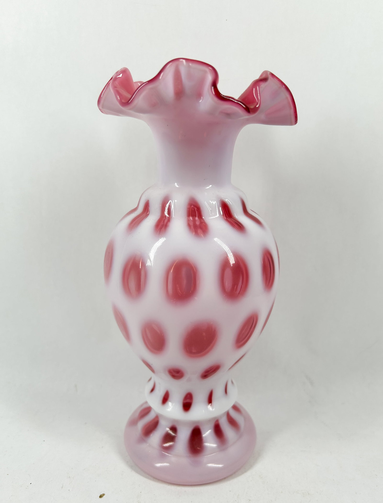 FENTON CRANBERRY OPALESCENT COIN DOT GLASS VASE: A cranberry opalescent glass vase featuring a bulbous body with a coin spot pattern and a ruffled rim. A small white rectangular adhesive label on the translucent base reads 85-.