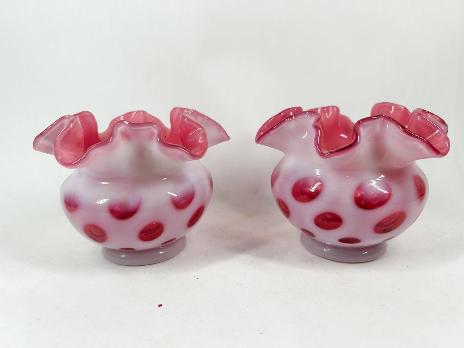 FENTON CRANBERRY OPALESCENT GLASS VASES COIN DOT: A pair of hand-blown cranberry opalescent glass vases featuring a recessed polka dot pattern and deeply ruffled rims. The center of each base features a circular ground and polished pontil mark; no