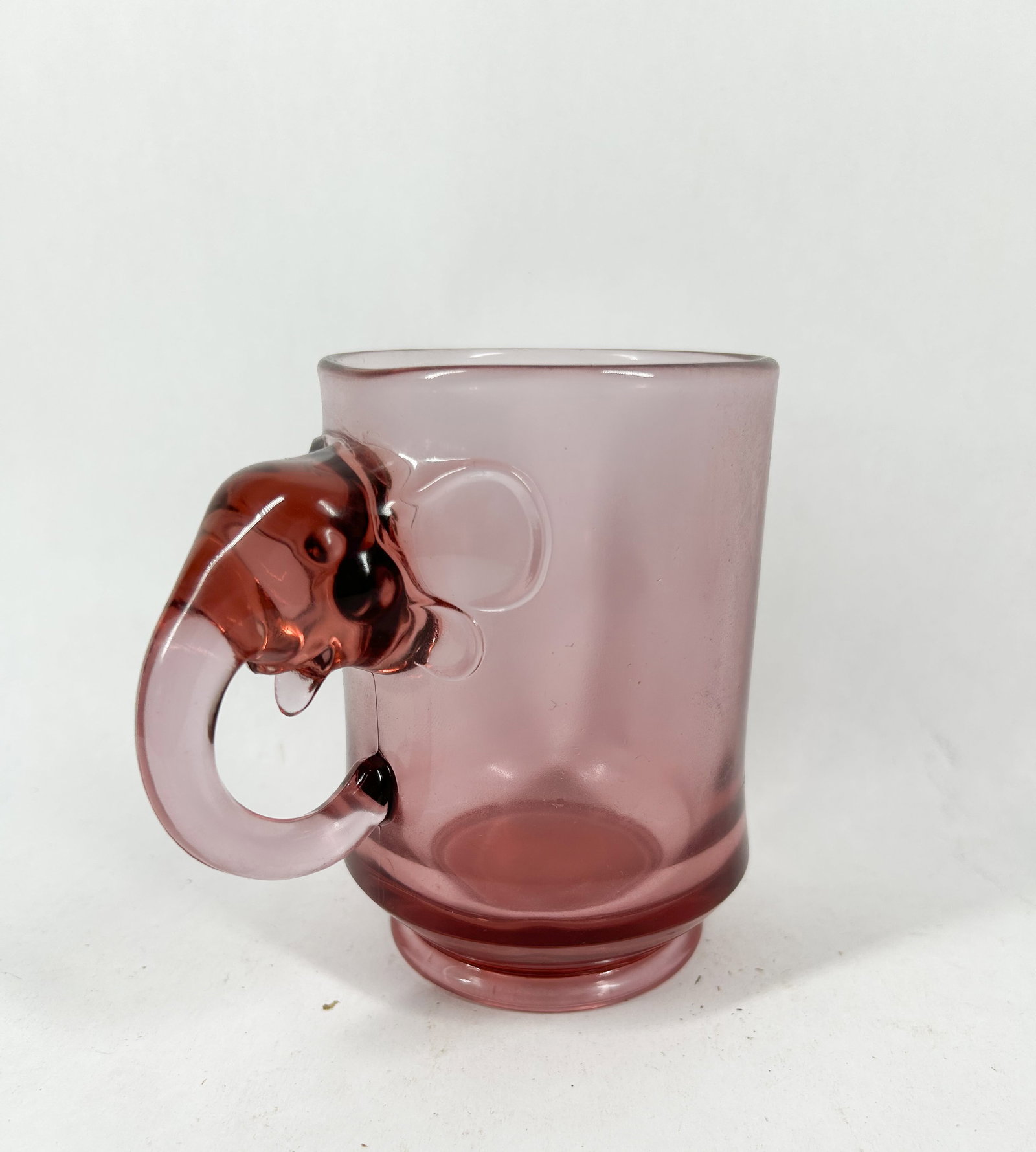 IMPERIAL GLASS PINK ELEPHANT MUG 1970: Pink pressed glass mug featuring a handle molded in the shape of an elephant head and trunk, produced by the Imperial Glass Corporation. The underside of the base is embossed with a top arc reading