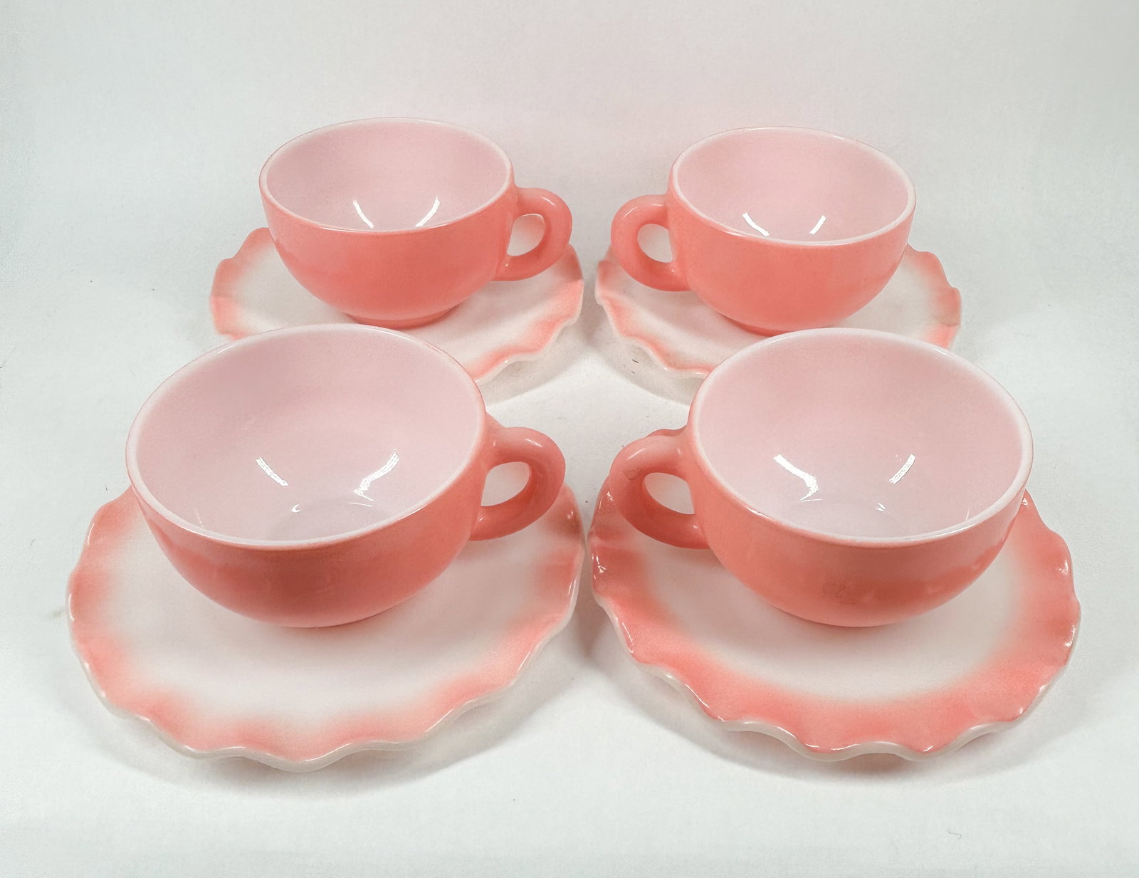 HAZEL-ATLAS PINK MILK GLASS SERVICE, MID-20TH CENTURY: A set of pink milk glass cups and saucers produced by the Hazel-Atlas Glass Company. Each piece features an embossed mark on the base consisting of a large letter H with a smaller letter A nested