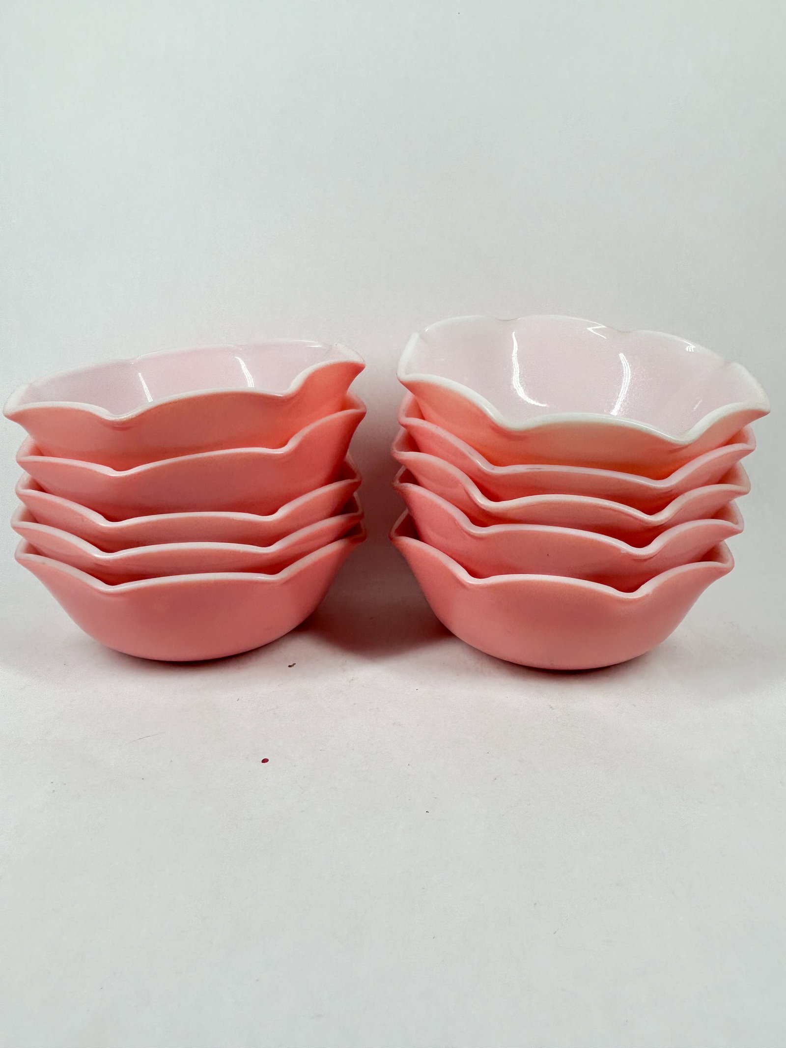 HAZEL ATLAS RUFFLED TABLEWARE: A set of ten milk glass dessert bowls featuring a fired-on pink exterior and a ruffled rim. The base of each piece bears an impressed mark consisting of a nested capital letter H and A, alongside the