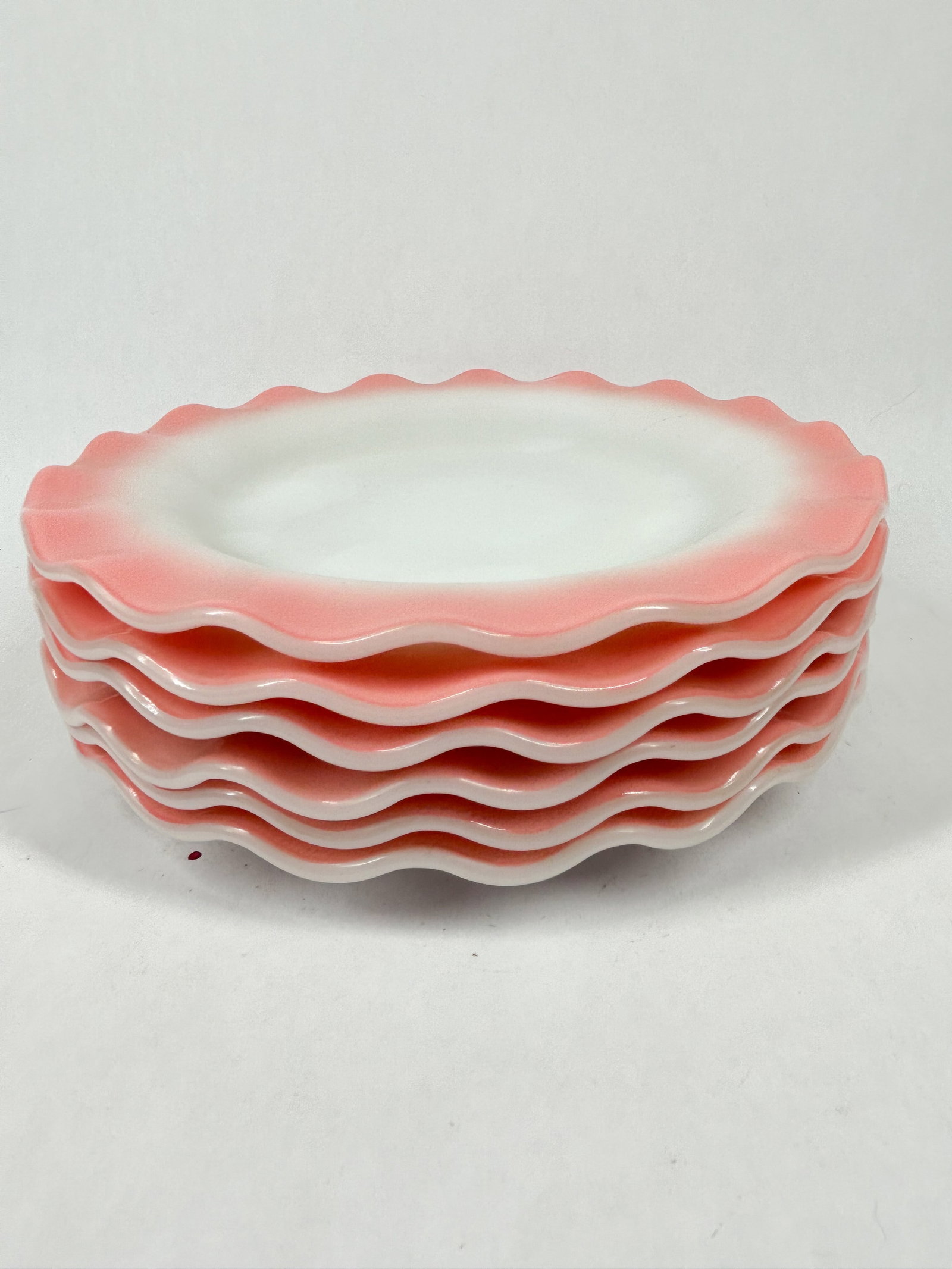HAZEL ATLAS RUFFLED PLATES: Set of five dessert plates in opaque white milk glass. Each piece features a factory-applied shaded pink border and a deeply scalloped ruffled rim. The base of each plate is smooth and unmarked.