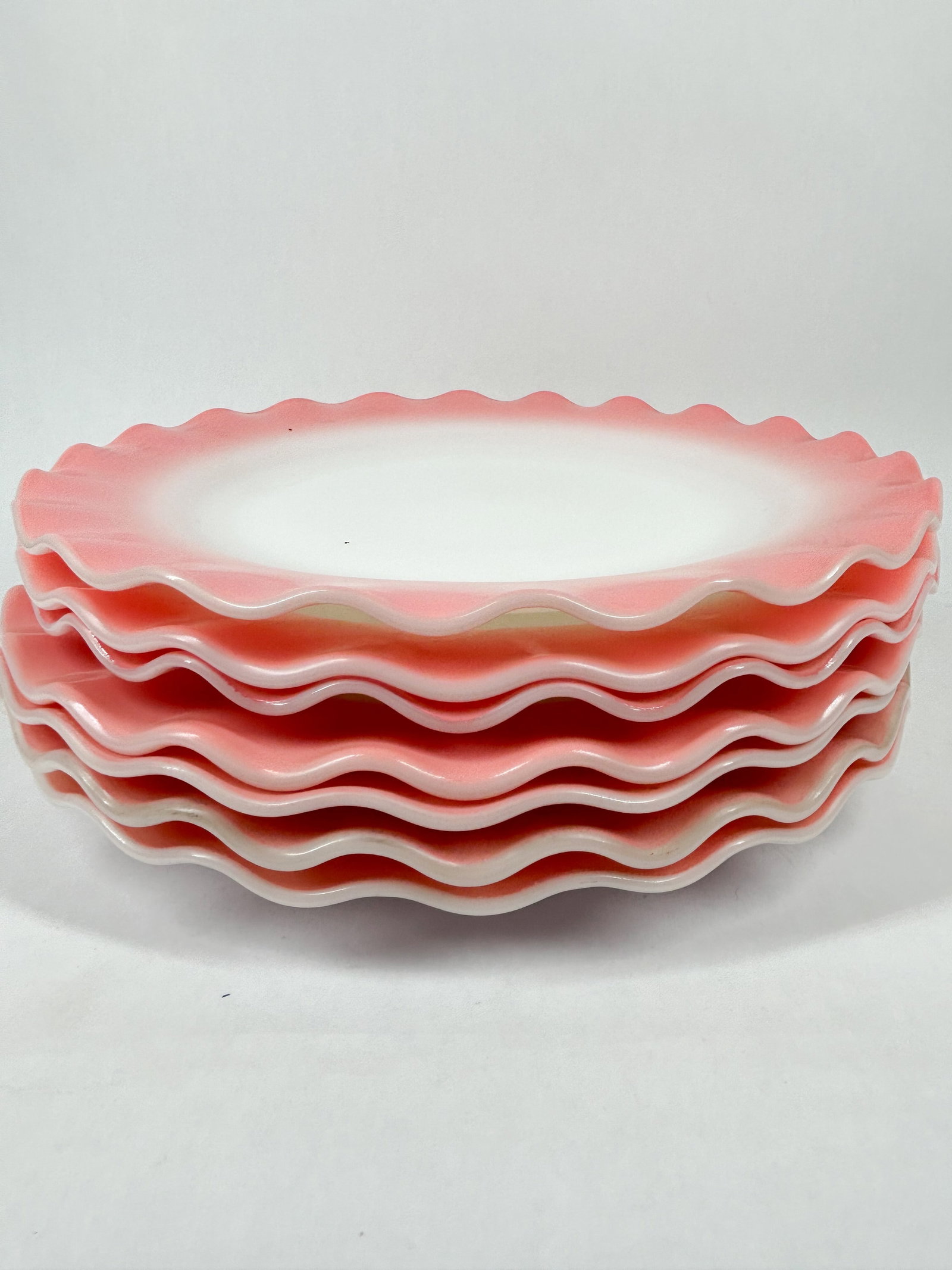 HAZEL ATLAS RUFFLED PLATES: A set of milk glass plates with ruffled rims and a fired-on pink ombre border. Each plate features a small embossed mark on the base consisting of the numerals 1 and 7.