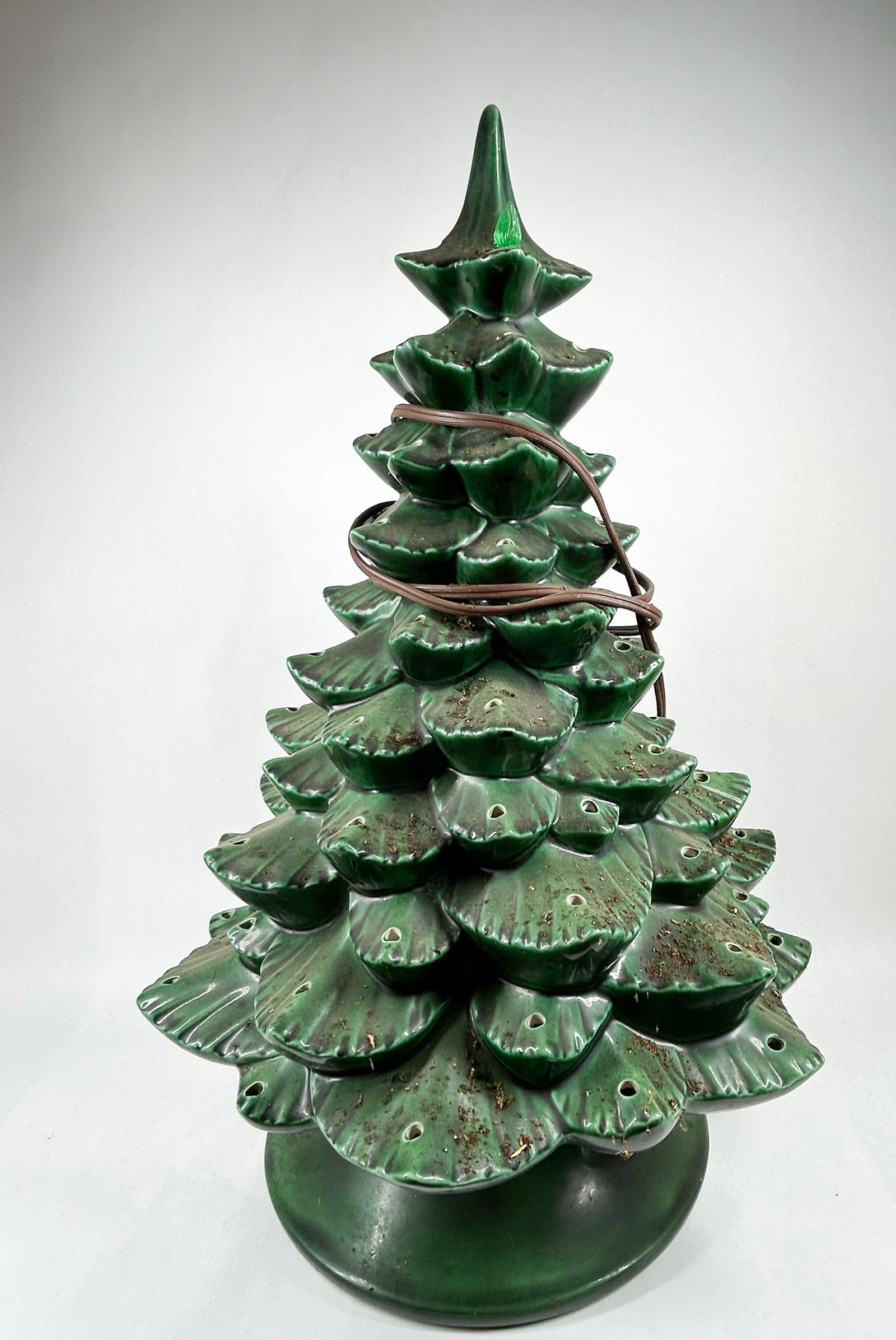 GLAZED CERAMIC CHRISTMAS TREE, MID-20TH CENTURY: A tiered ceramic Christmas tree finished in a forest green gloss glaze with dark brown accents to the branch tips. The piece consists of a main tree body atop a matching flared circular base and