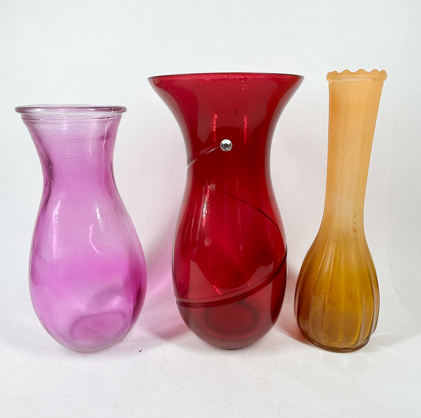 TELEFLORA AND ASSORTED GLASS VASES: A trio of glass vases including a red Teleflora gift vase with a spiral wrap and an applied clear glass accent. The red vase base bears a printed mark with a rose graphic, DIAMONDS & ROSES, teleflora