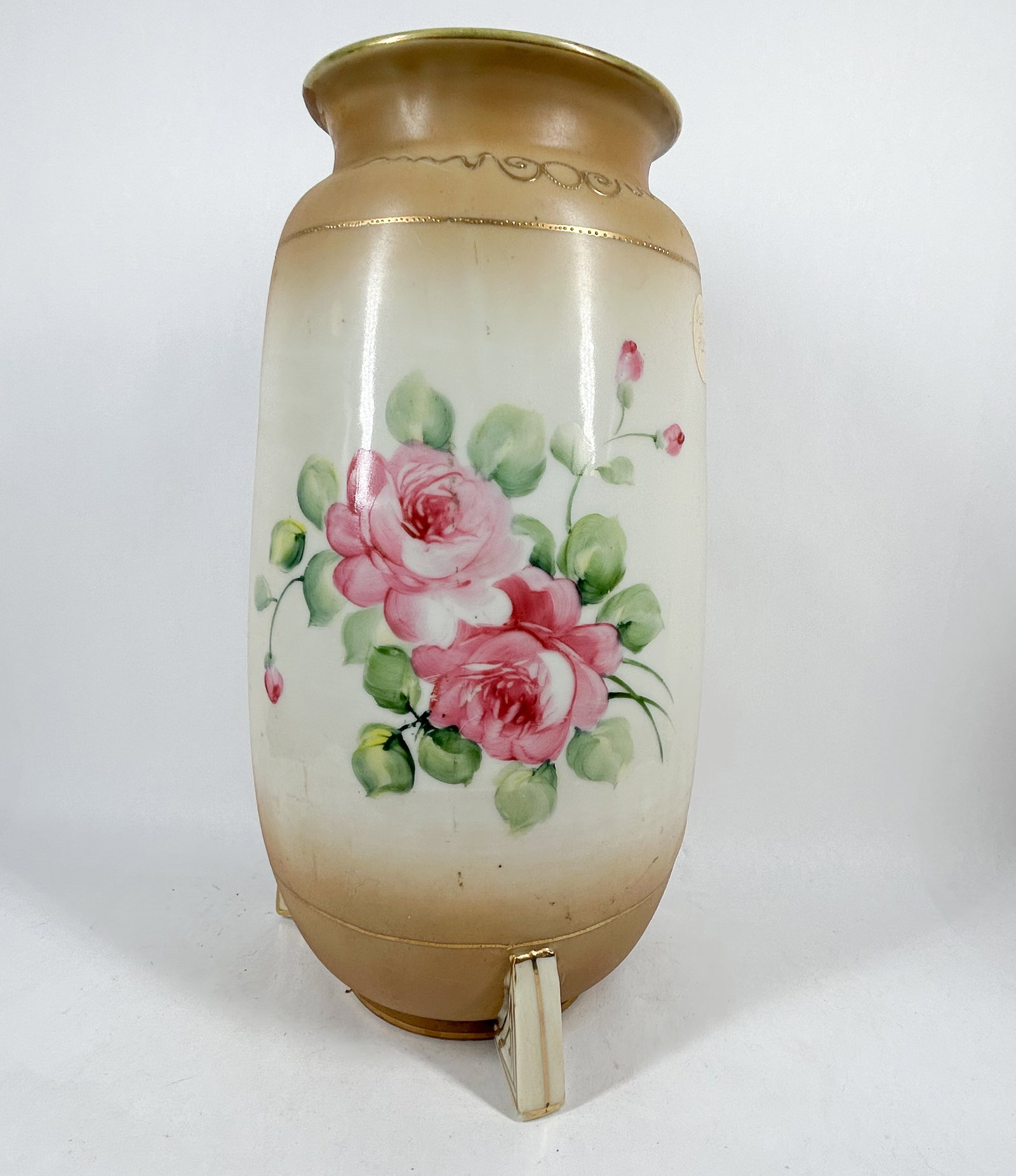 NIPPON PORCELAIN VASE, CIRCA 1910: Japanese Nippon porcelain vase featuring three scroll feet and dual-sided hand-painted decoration of roses and a mountain landscape with raised gold moriage detailing. A green printed mark on the unde