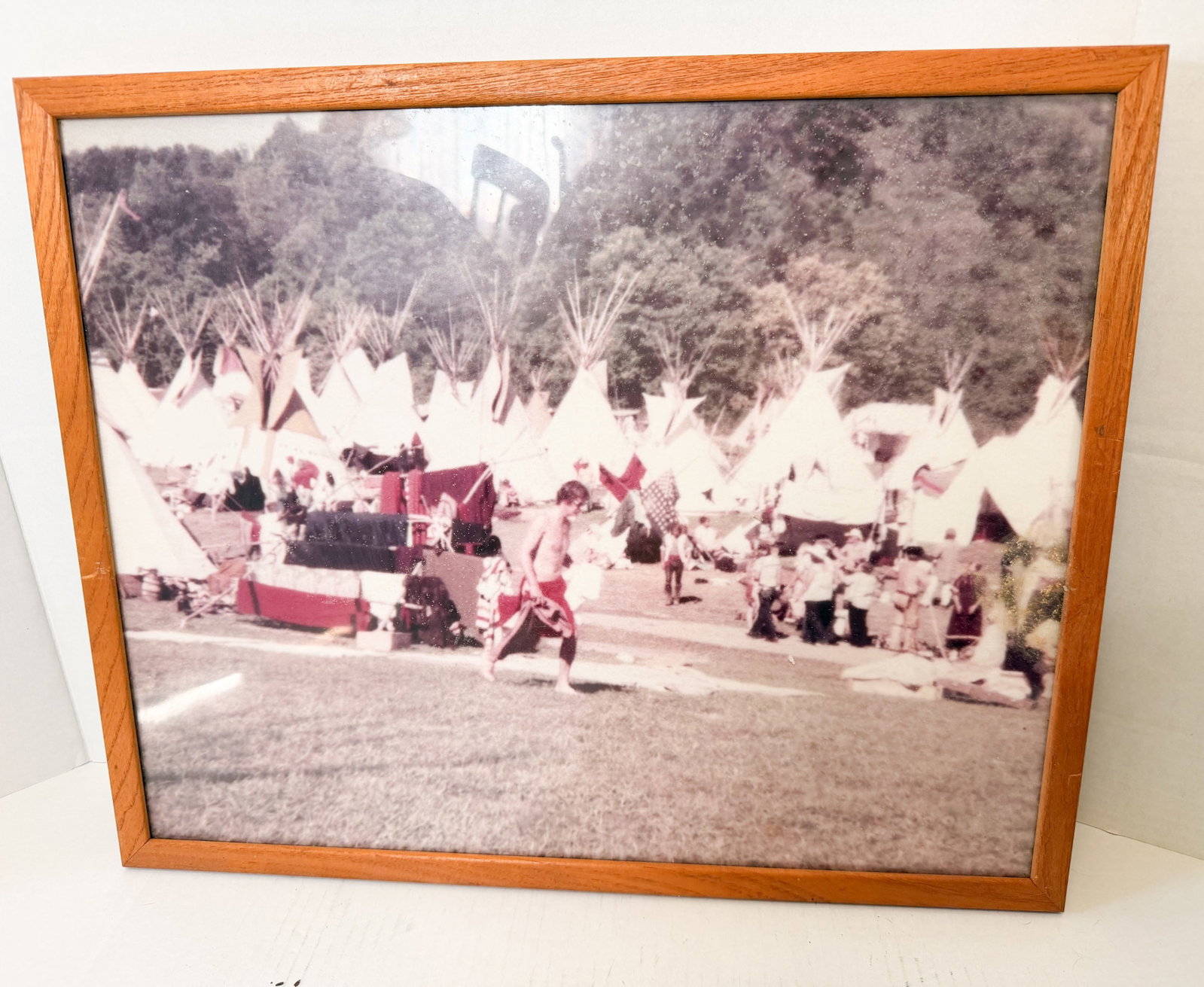VINTAGE TIPI ENCAMPMENT C-PRINT PHOTOGRAPH: A vintage chromogenic print depicting a large-scale tipi encampment at the base of a wooded hill. The documentary-style scene shows various figures and supplies dispersed through the campsite, present