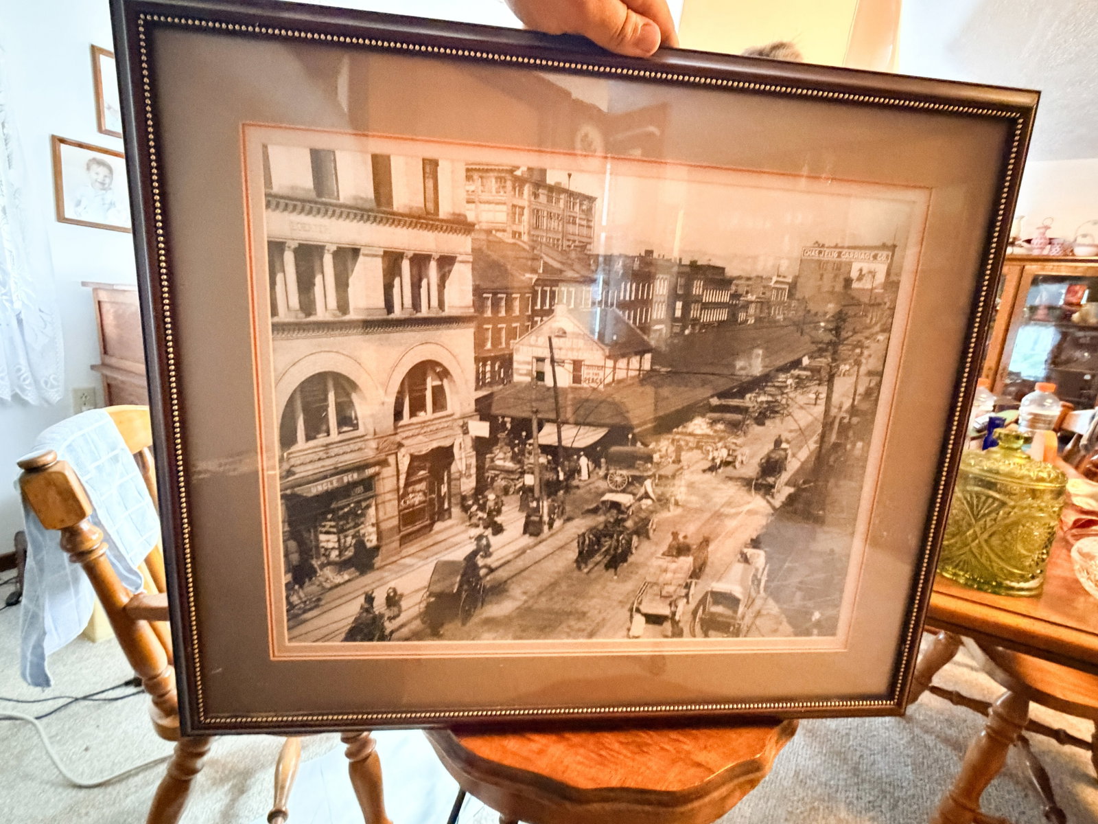 WHEELING MARKET PLAZA FRAMED PRINT, C. 1900: A framed monochrome print depicting the historic Market Plaza in Wheeling, West Virginia, during the late 19th century. The bustling street scene features horse-drawn carriages and period commercial s