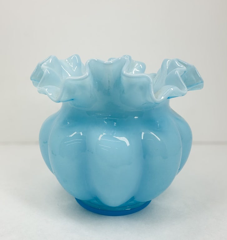 FENTON BLUE OVERLAY MELON VASE: A vintage light blue cased glass vase produced by Fenton Art Glass Company featuring a lobed melon form and a wide ruffled rim. An embossed oval Fenton logo is visible on the interior base of the vess