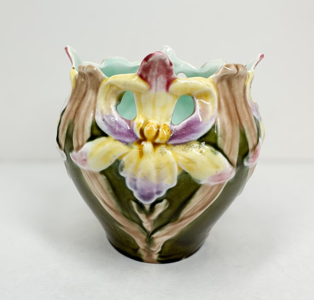 MAJOLICA IRIS VASE: Art Nouveau majolica vase featuring high-relief molded iris decoration against an olive green ground with a turquoise glazed interior and a reticulated rim. The unglazed base is impressed with numeral
