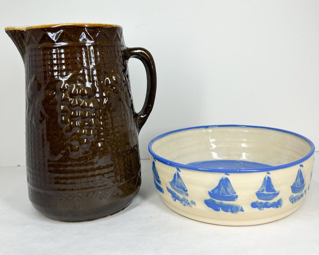 JUDY LONGTON BOWL AND STONEWARE PITCHER: Studio pottery bowl by Judy Longton featuring cobalt blue sailboats and sgraffito decoration, accompanied by a relief-molded stoneware pitcher with grape and lattice motifs. The bowl base bears the in