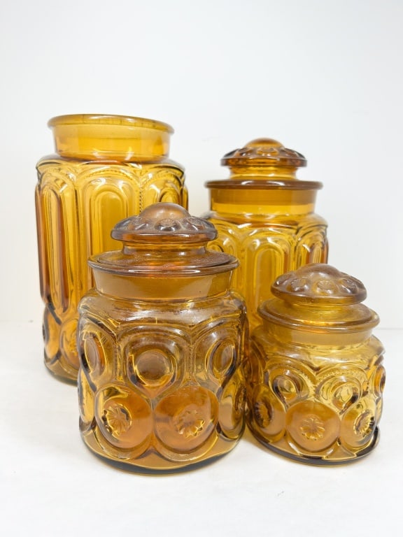 AMBER MOON AND STAR GLASS CANISTERS: A set of four amber pressed glass canisters featuring the Moon and Star pattern. The cylindrical bodies display characteristic circular indentations and starburst motifs below domed lids.